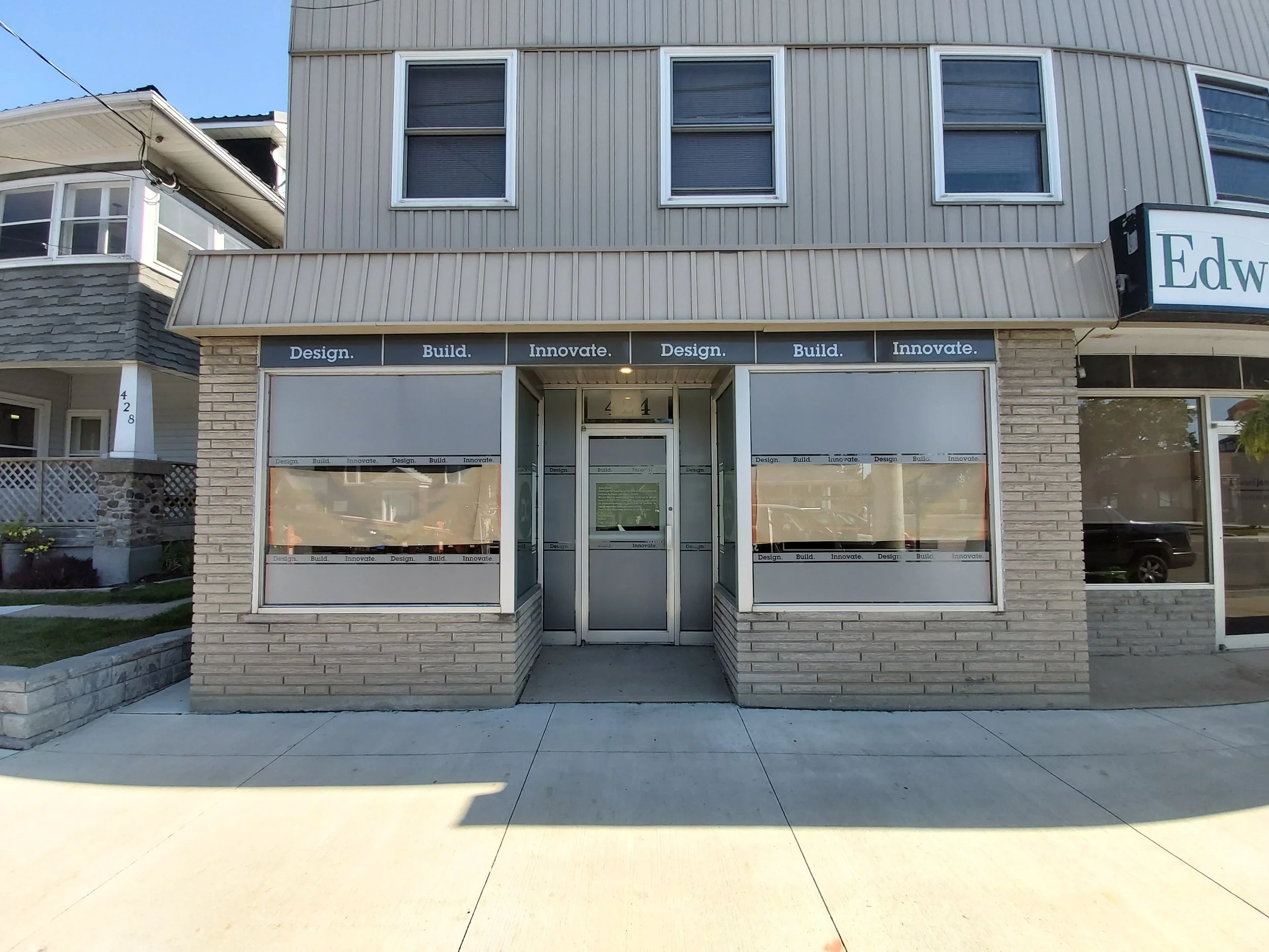 Empty storefront with large windows covered with protective paper and a glass door, located in a beige brick building with gray siding on the upper level.