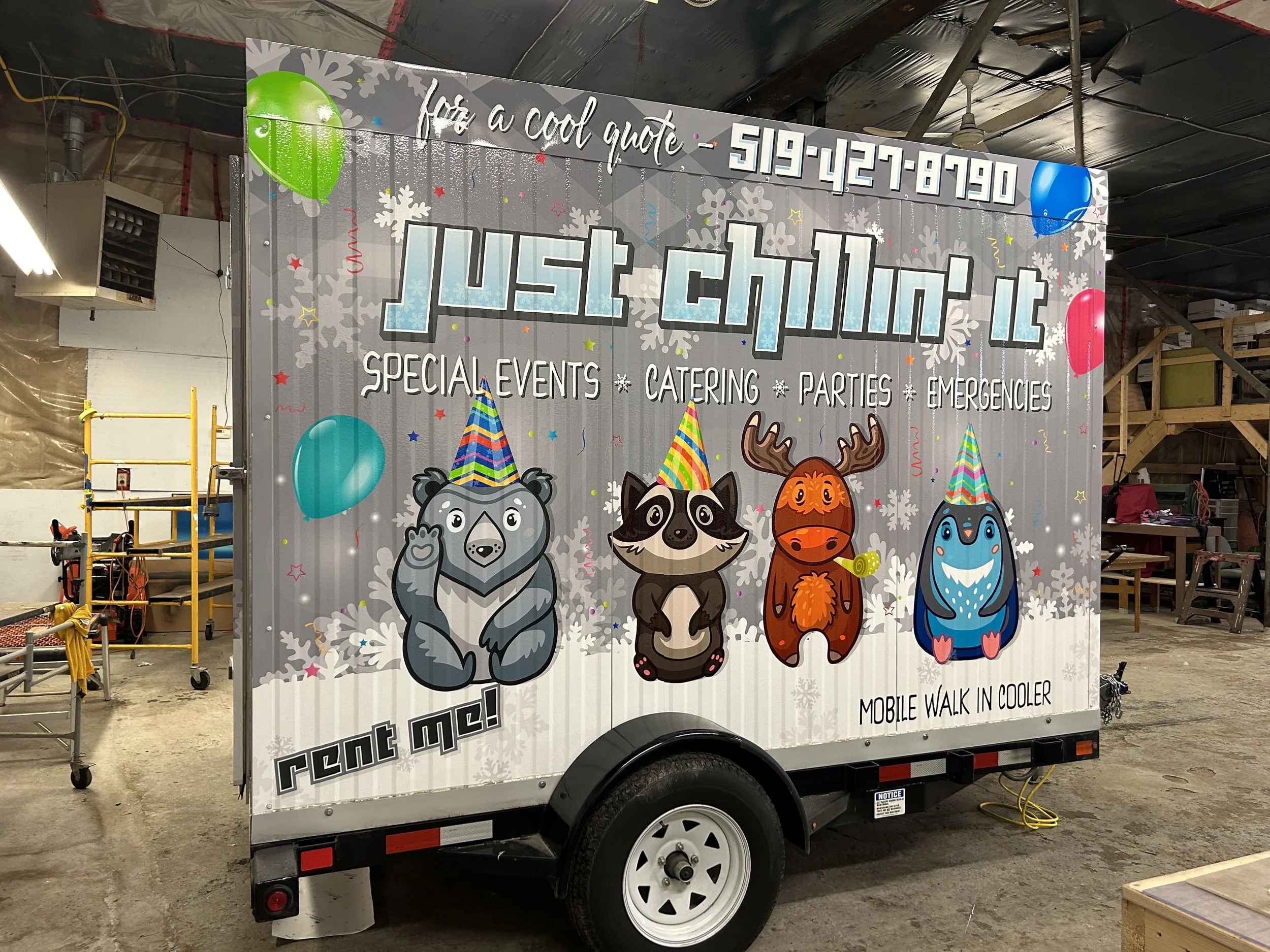 A decorated trailer with cartoon animals wearing party hats advertising a mobile cooling unit for events, catering, parties, and emergencies, featuring colorful balloons, snowflakes, and the company's contact number.