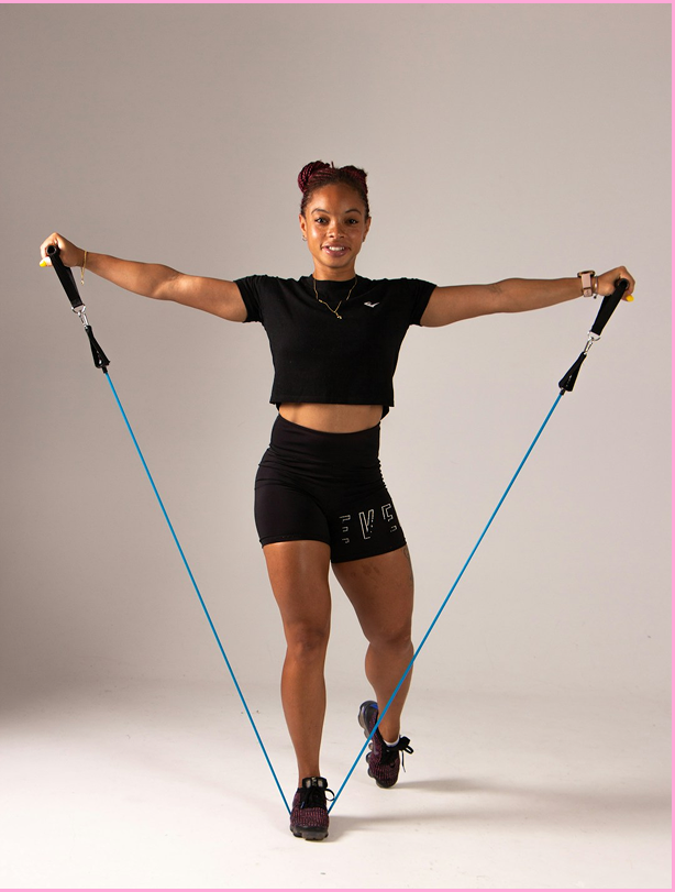 A woman exercises with resistance bands in a studio with a plain background.