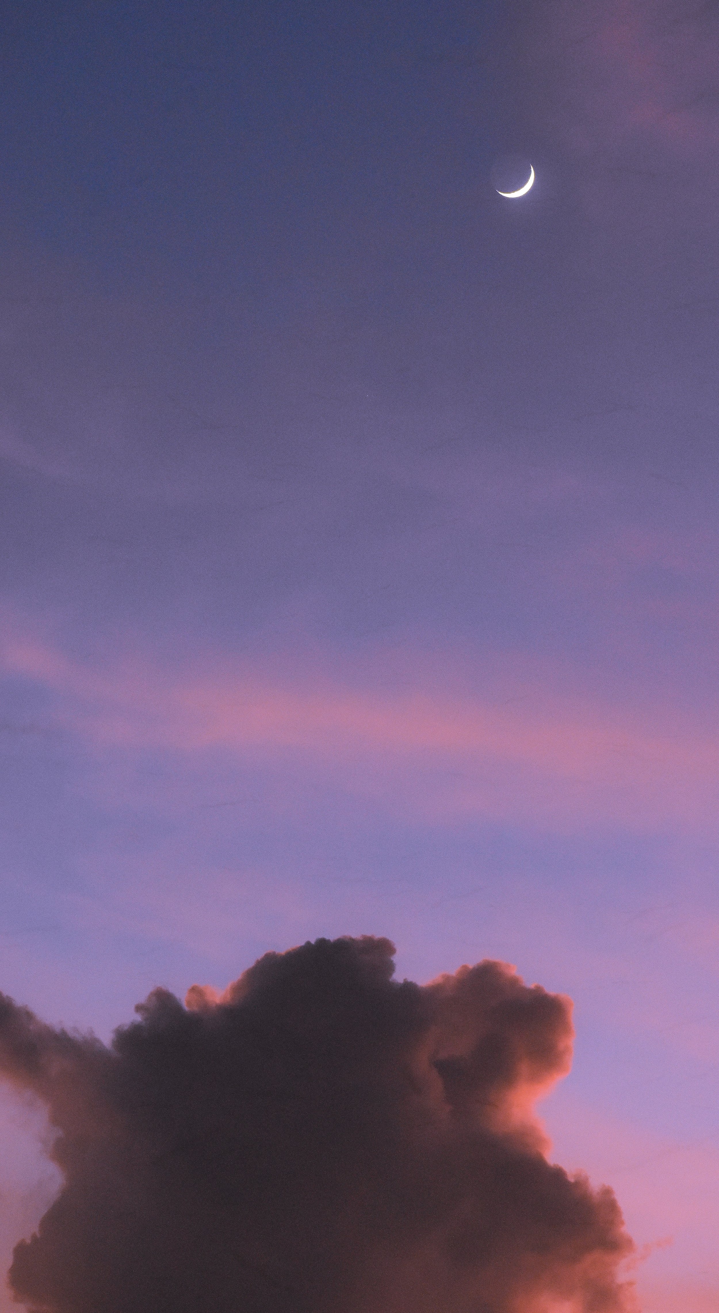 A view of a purple sky during sunset with a crescent moon in the top right corner and dark clouds at the bottom.