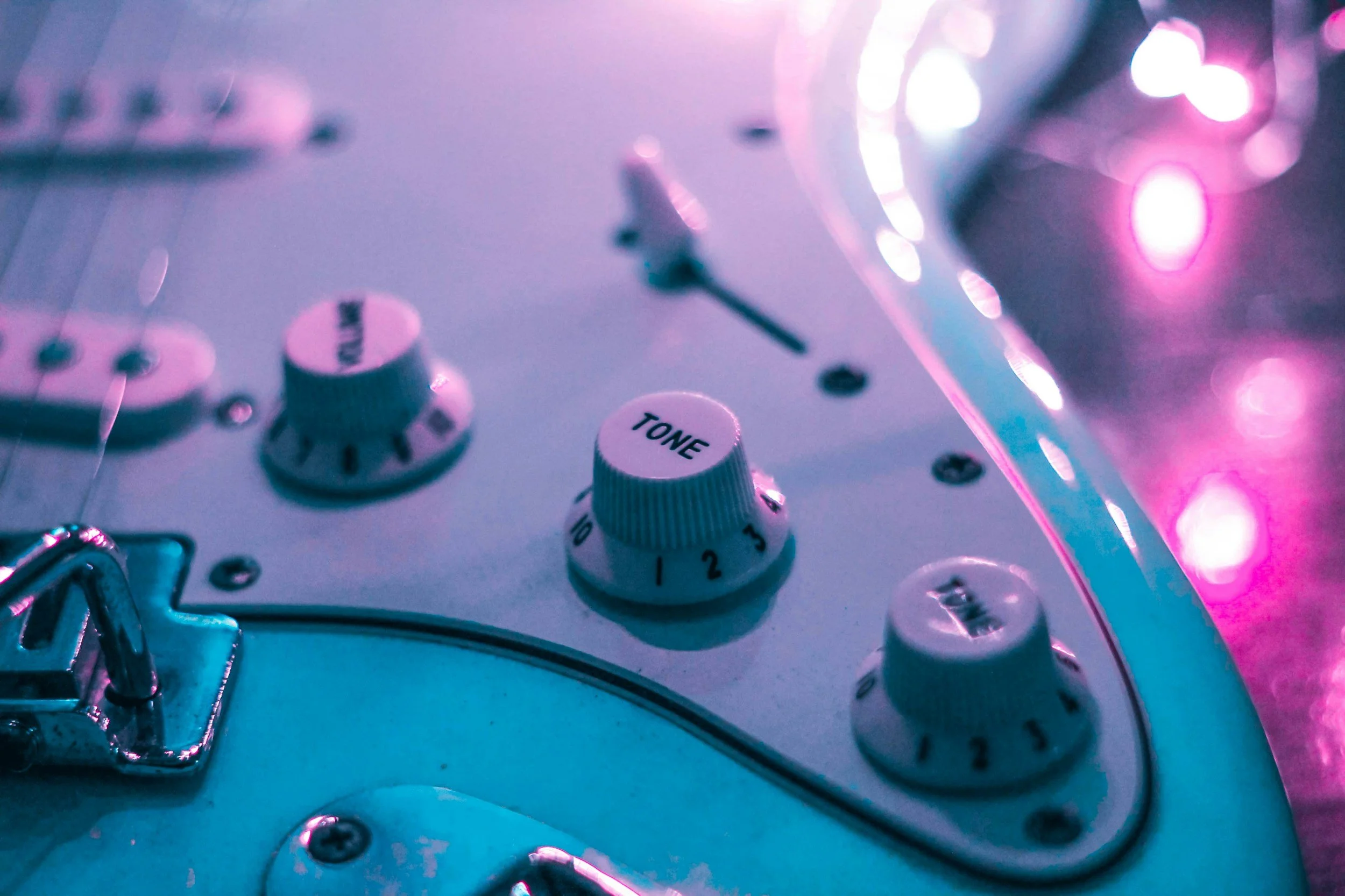Close-up of a guitar amplifier with tone control knob, set to about 2, under pink and purple neon lighting.