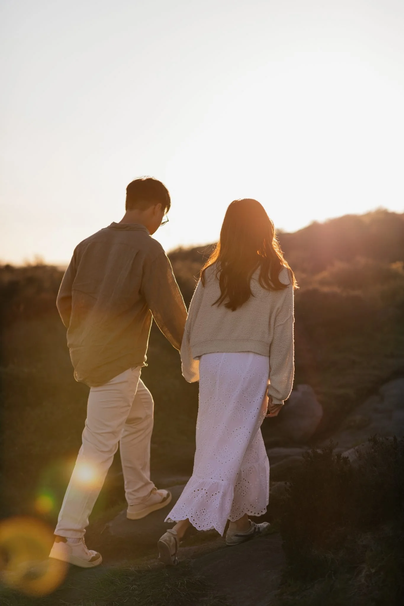 A couple holding hands and walking outdoors during sunset with a mountain in the background
