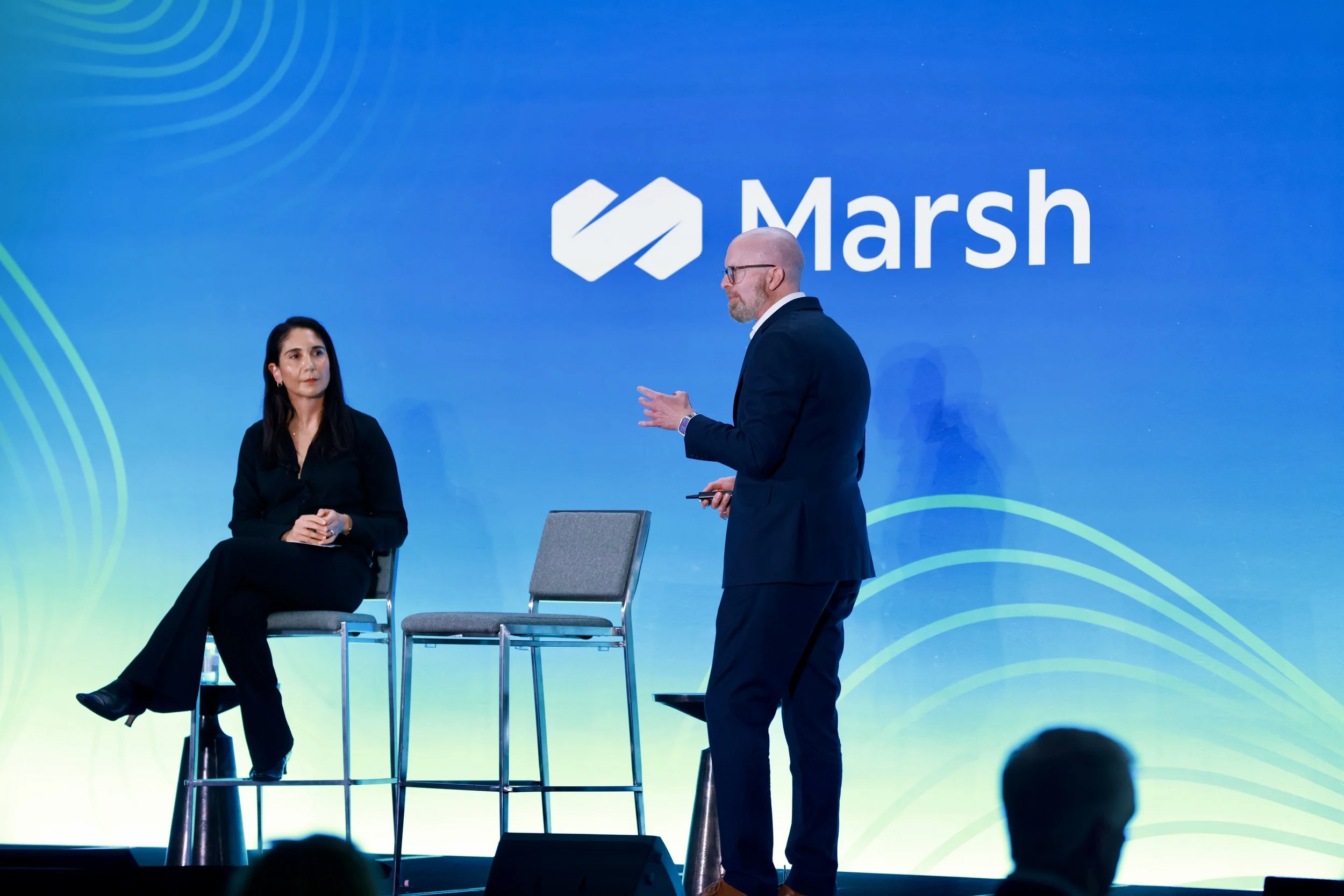 Daniel Kaniewski addresses the Marsh Real Estate and Hospitality Conference. The stage background features the Marsh logo and a blue gradient design.