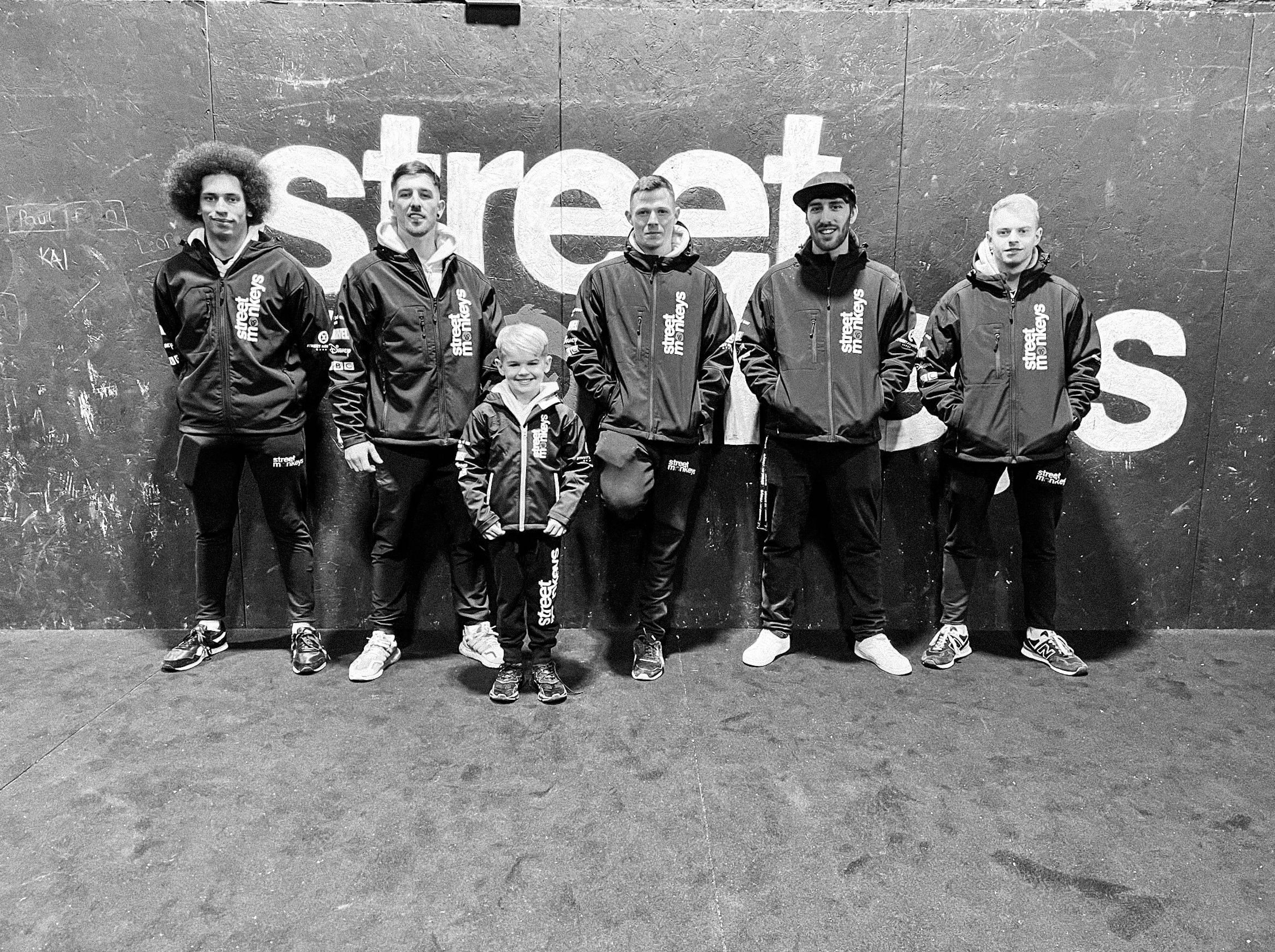 Group of six people, including a young boy, standing in front of a wall with the word 'street' on it. They are all wearing matching jackets with 'street me' on them.