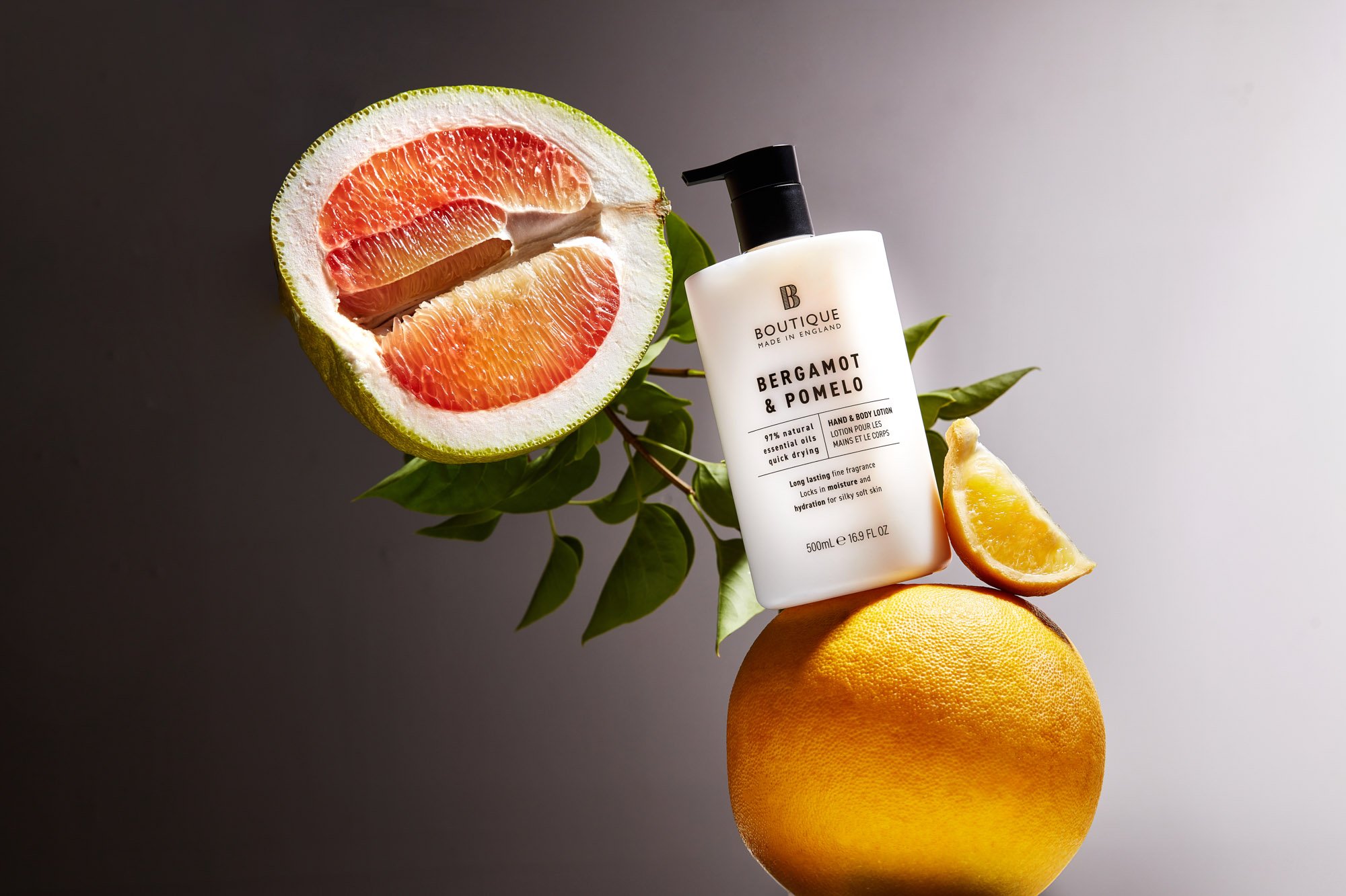 A skincare lotion bottle labeled 'Bergamot & Pomelo' amidst grapefruit, lemon, and leaves