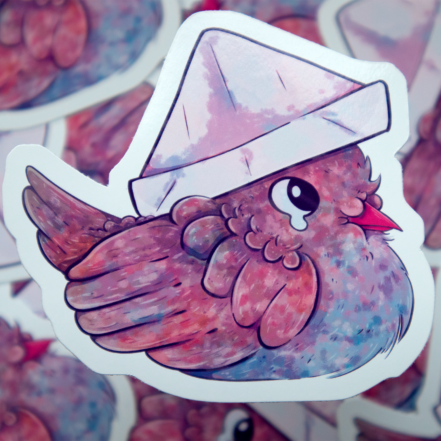 A sticker illustration of a chubby pigeon with fluffy feathers, big teary eyes, and a blue marking on it's breast. It's wearing a white paper folded hat on it's head.