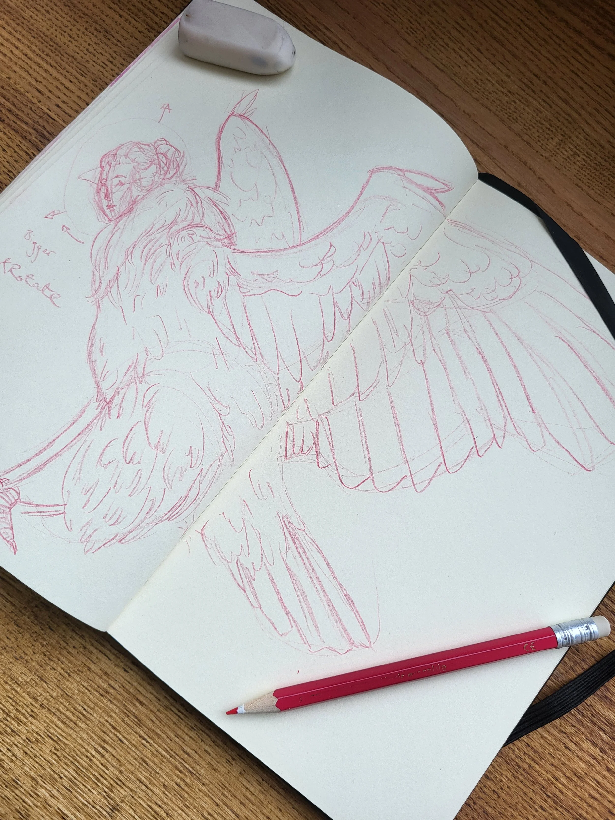 Sketch of a siren from Greek Mythology, a creature with the body of an eagle and the face of an attractive lady, in a sketchbook on a wooden table with a red pencil and an eraser nearby.