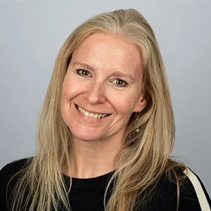 A woman with long blonde hair smiling at the camera, wearing a black top against a light background.