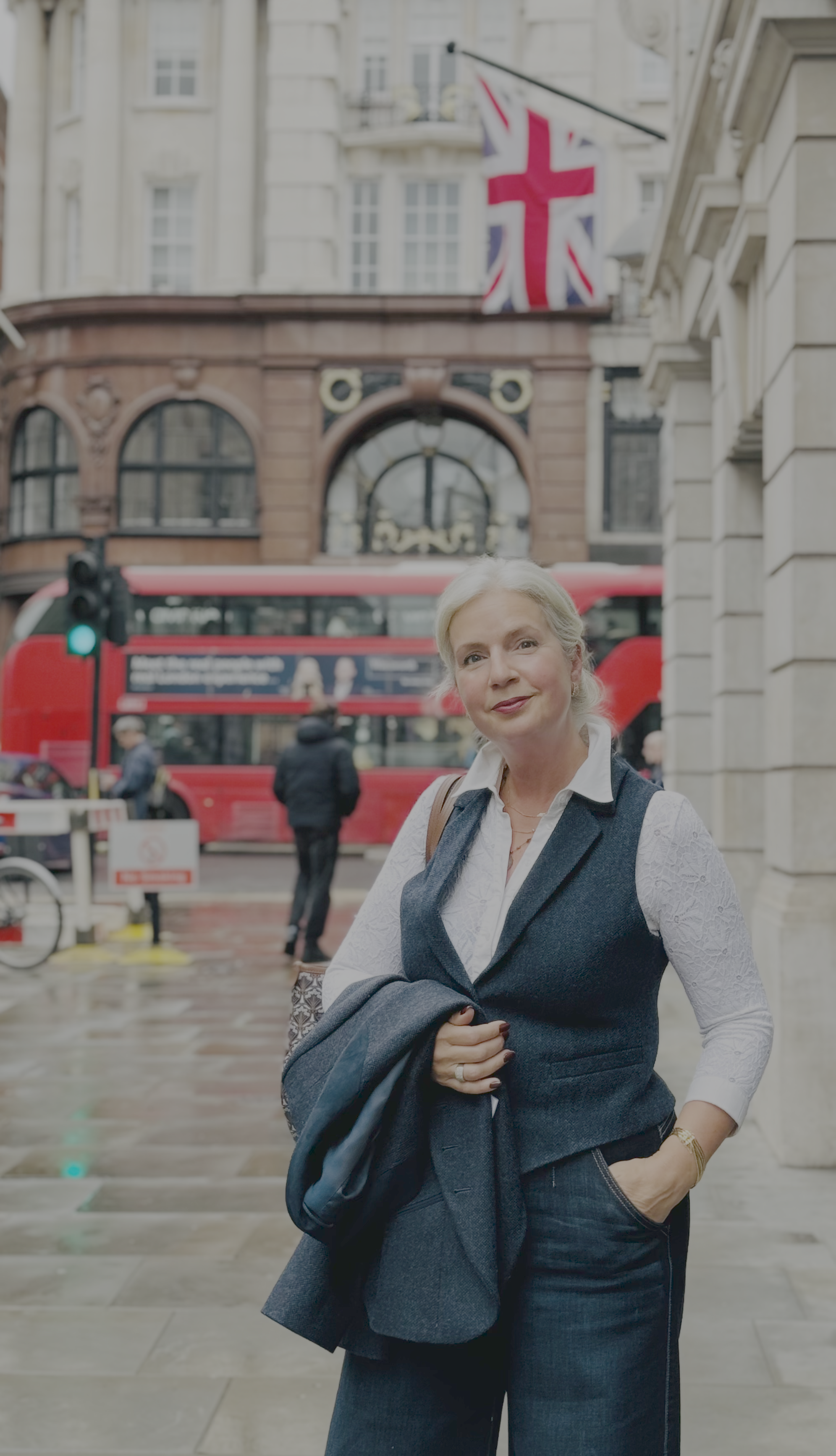 A woman standing on a city street with a double-decker bus and a Union Jack flag in the background.