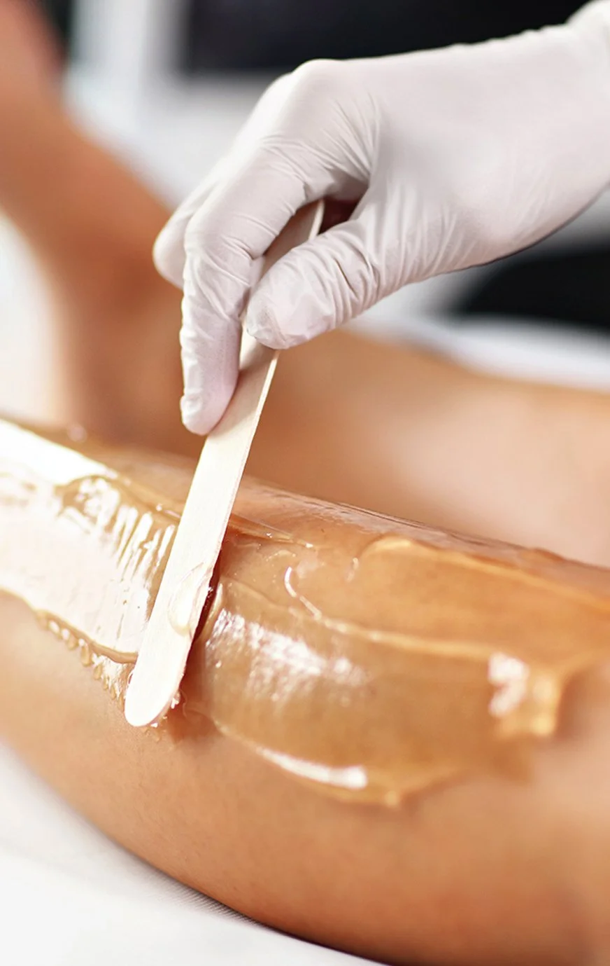 A person in a white glove applies wax to a person's leg during a waxing treatment.