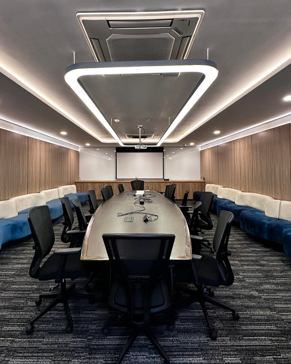 Conference room with long meeting table, ergonomic chairs, sofa furniture placed along the wall, and ambient lighting.