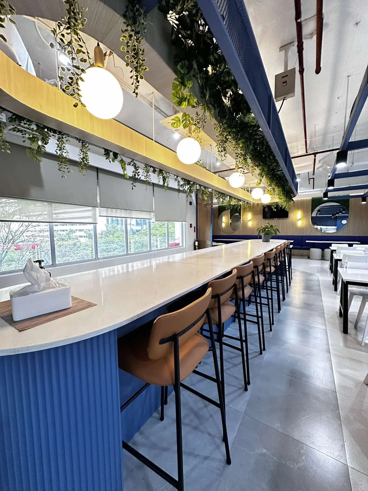 Modern communal space with high counter seating, pendant lights, and ceiling greenery accents.