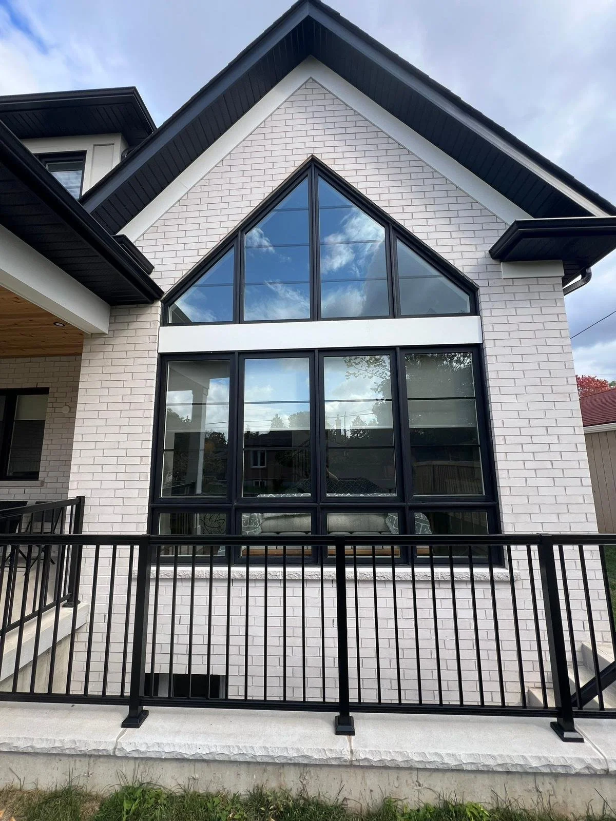 Modern house with white brick exterior, large black-framed glass windows and a triangular glass front, black roof, and a black metal railing in front.