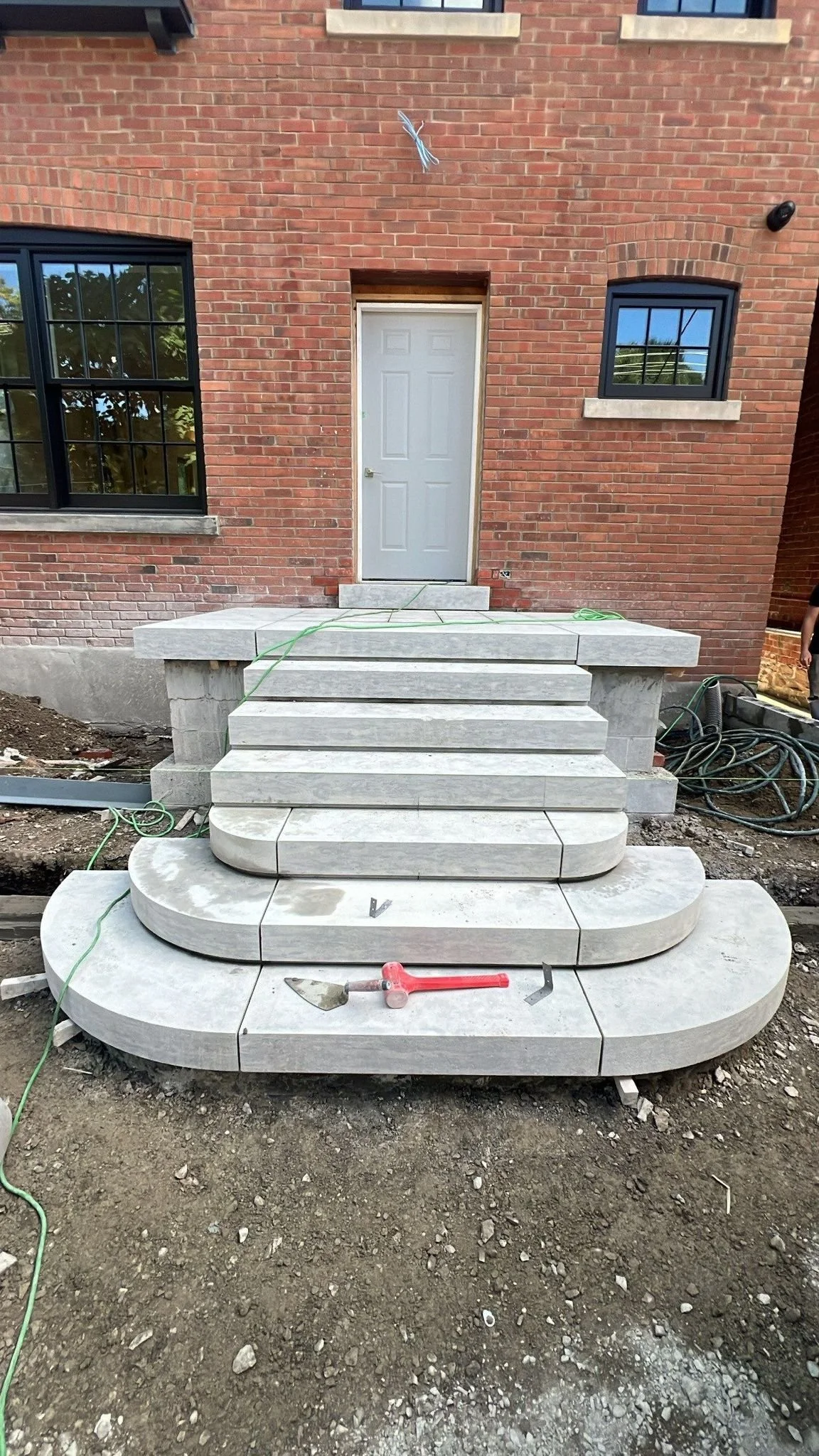 Stone staircase leading to a door at a construction site with dirt around it, and tools placed on the steps.