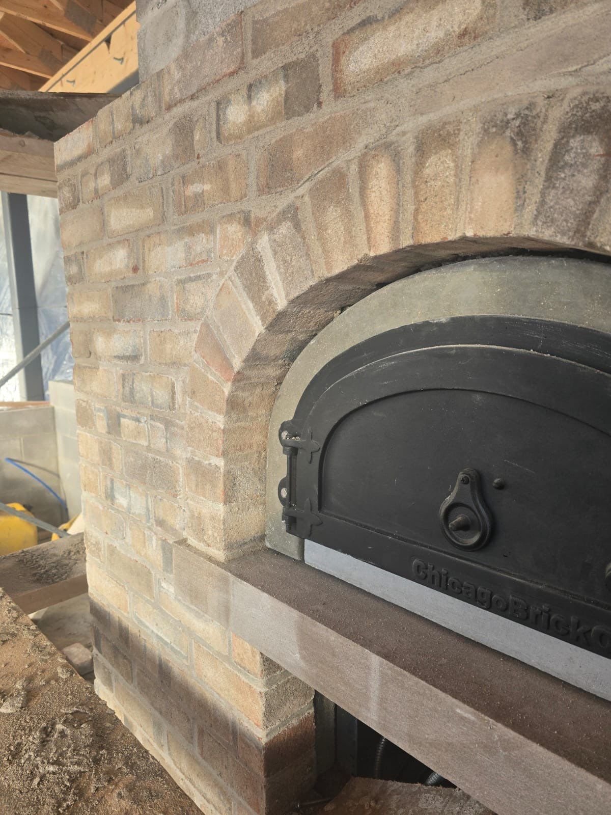 Close-up of a brick fireplace with a black metal oven door, under construction indoors.