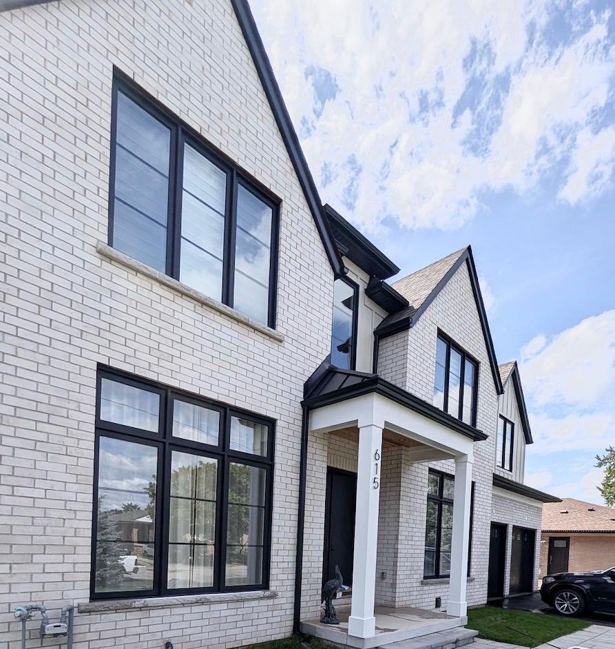 New two-story white brick house with black trim and multiple large windows, front porch with white columns, and a black car parked in driveway.