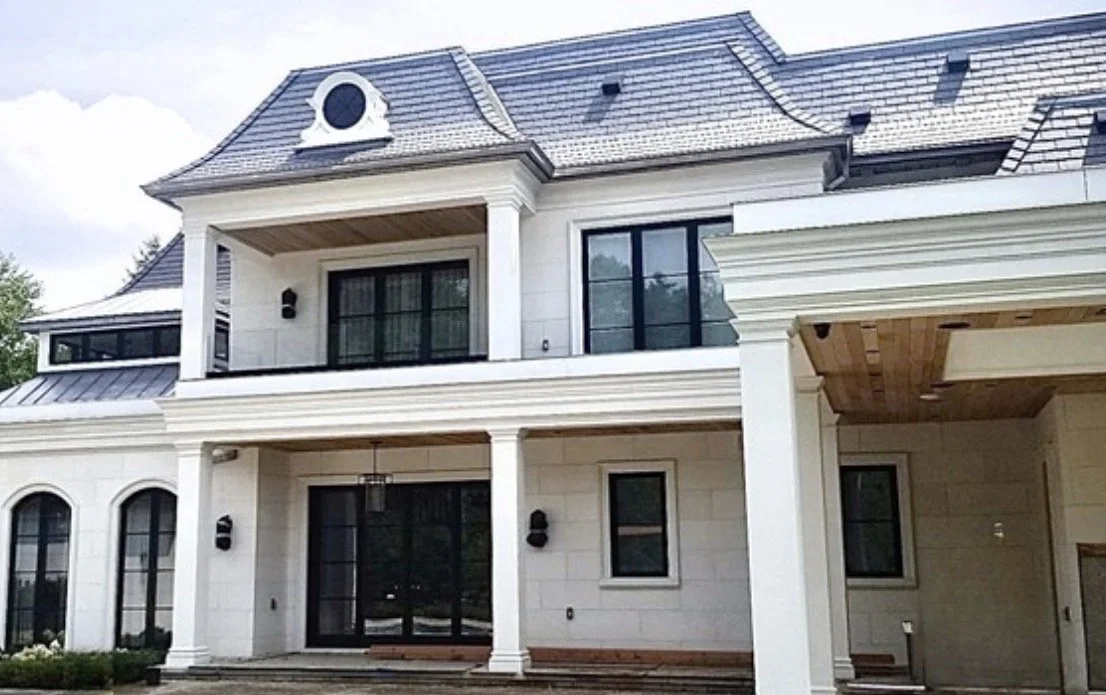 Front view of a large white house with multiple windows, columns, and a sloped roof with dormer windows.