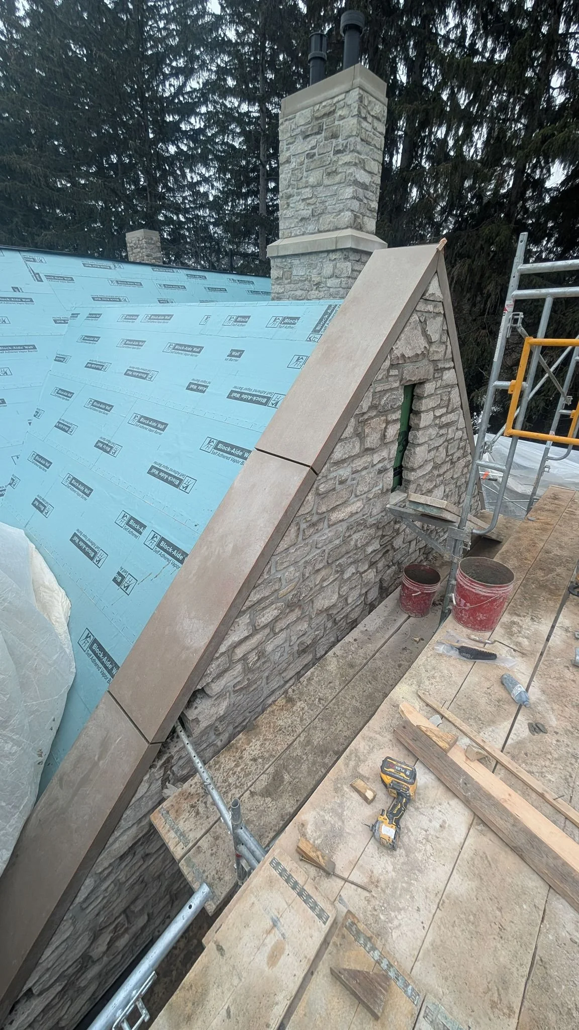 Undergoing roof construction, showing a sloped stone wall with beige tiles, scaffolding, and construction tools and buckets.