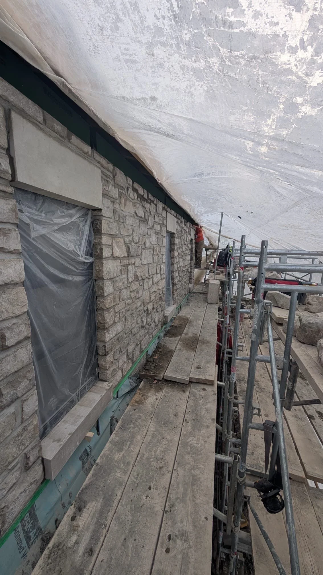 Construction site with brick wall and scaffolding, workers installing or repairing exterior wall of a building.