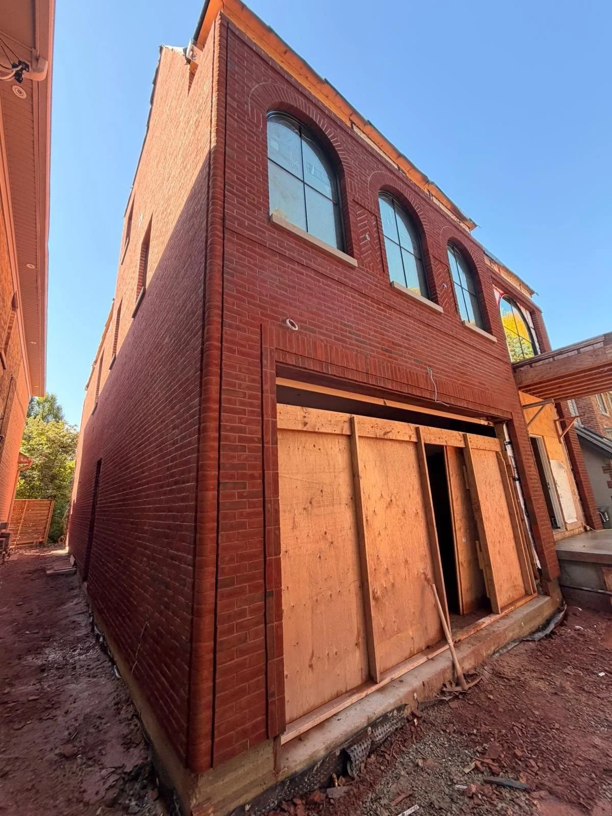 Three-story brick building under construction with wooden framing around ground floor entrance, and large arched windows on upper floors.