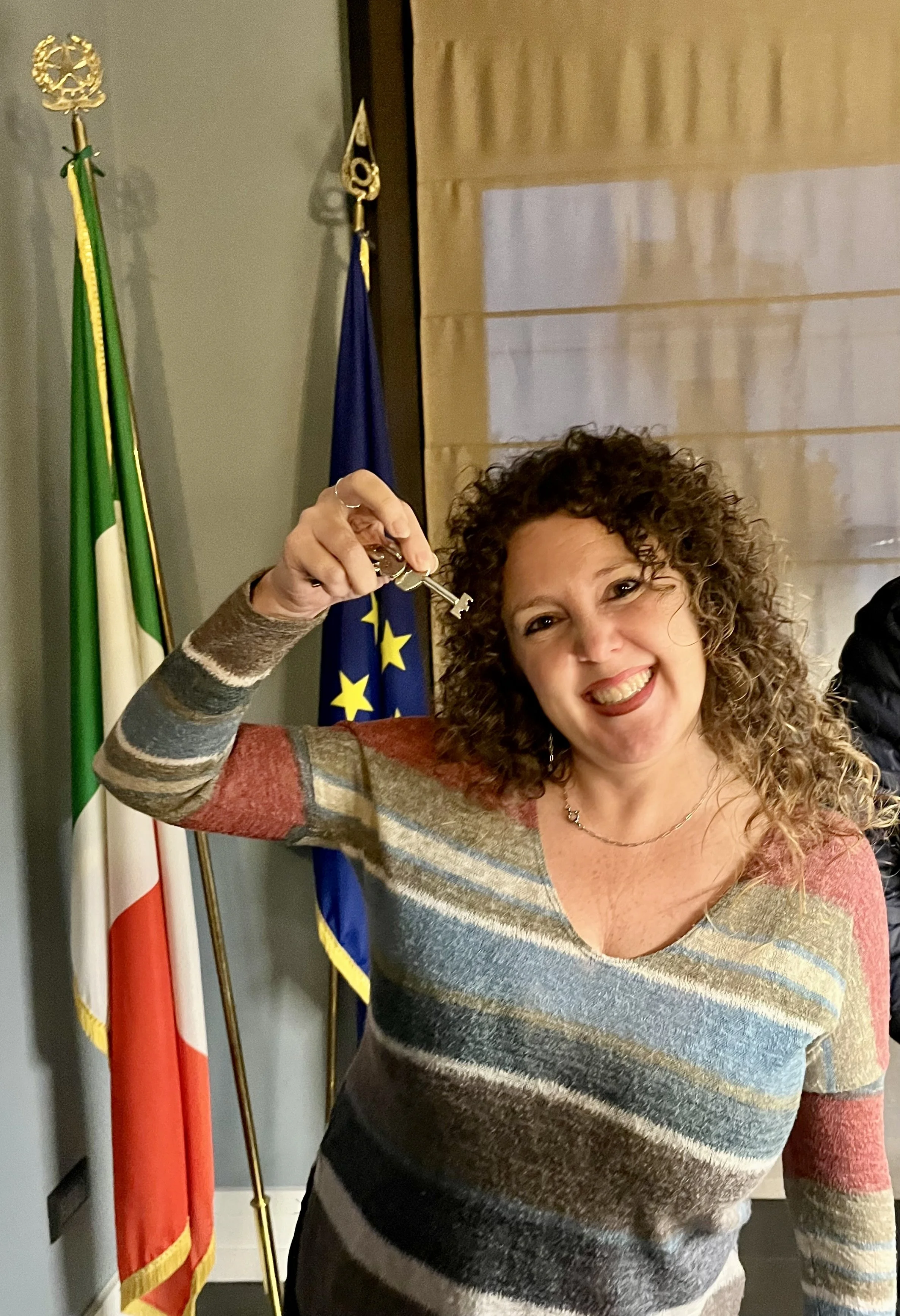 A young woman with curly hair holding a key next to an Italian flag.
