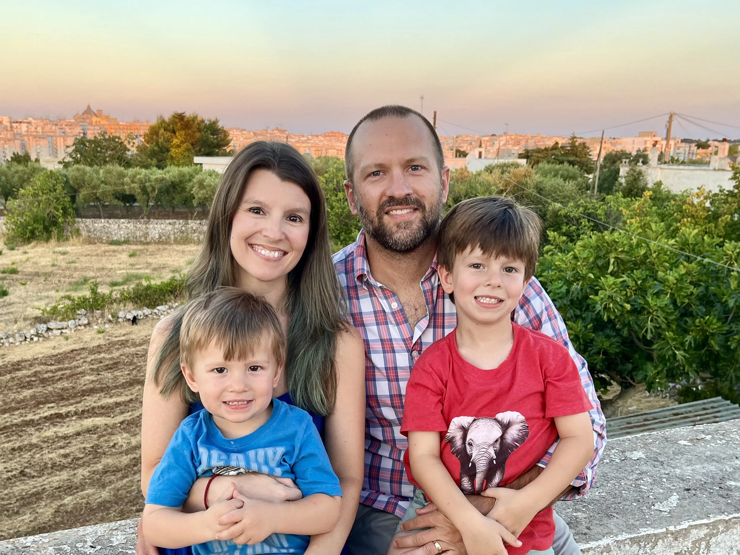 A young family smiling at a camera with a view of the valley and stone walls during sunset.