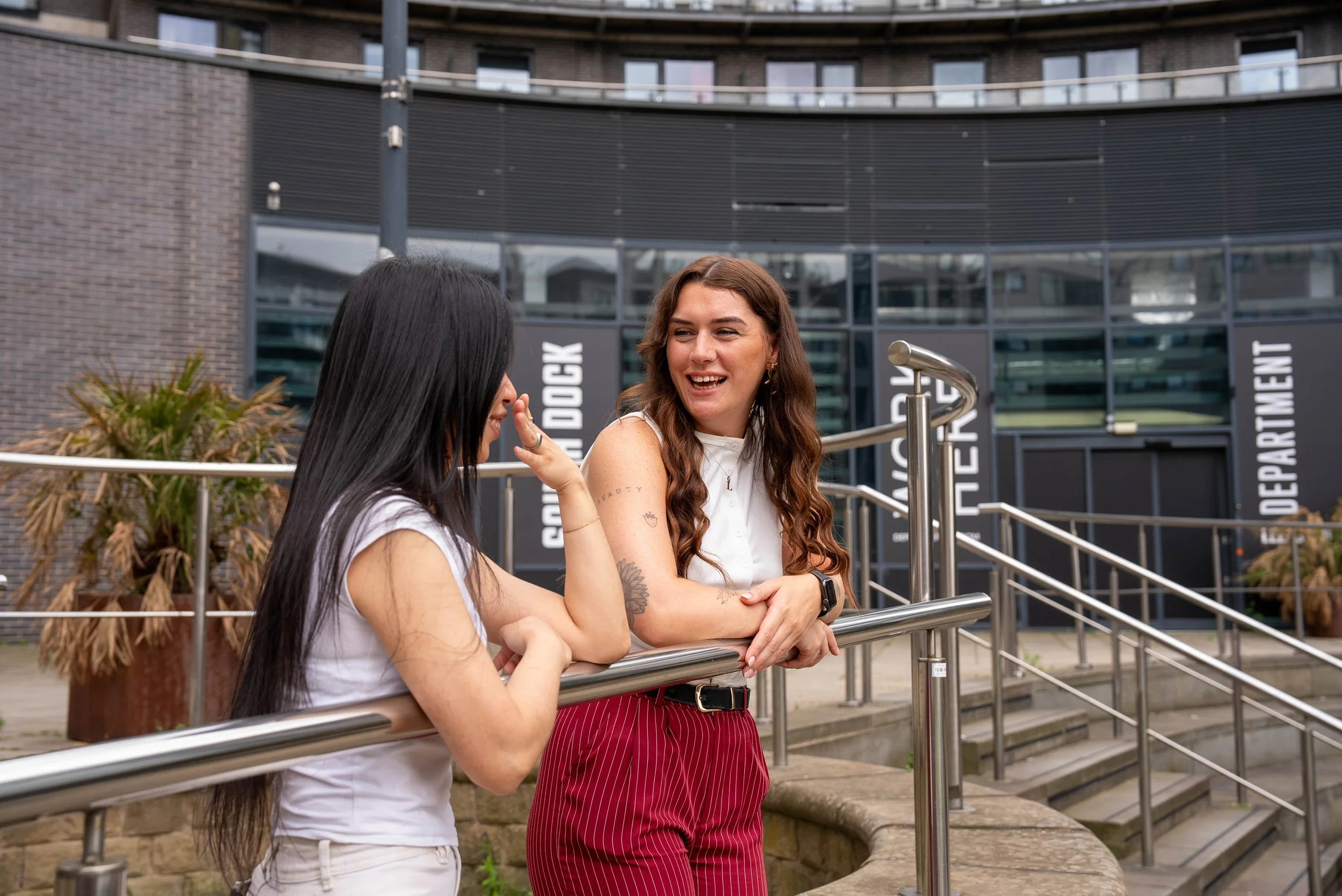 Lily Deal chatting outdoors near a modern building with stairs and landscaped plants.