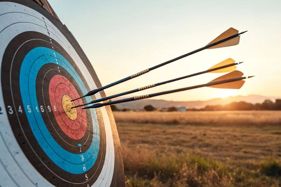 Three arrows stuck in the bullseye of a target outdoors at sunset.