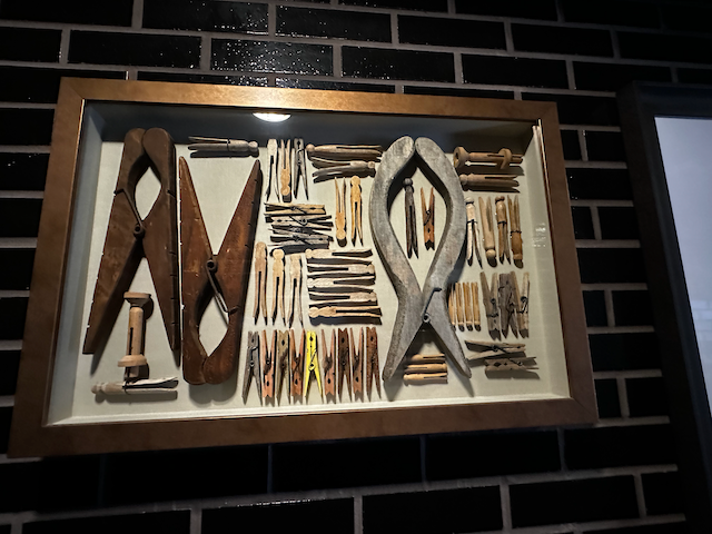 A framed display of various old hand tools, including pliers, scissors, and other woodworking or metalworking tools on a dark brick wall.