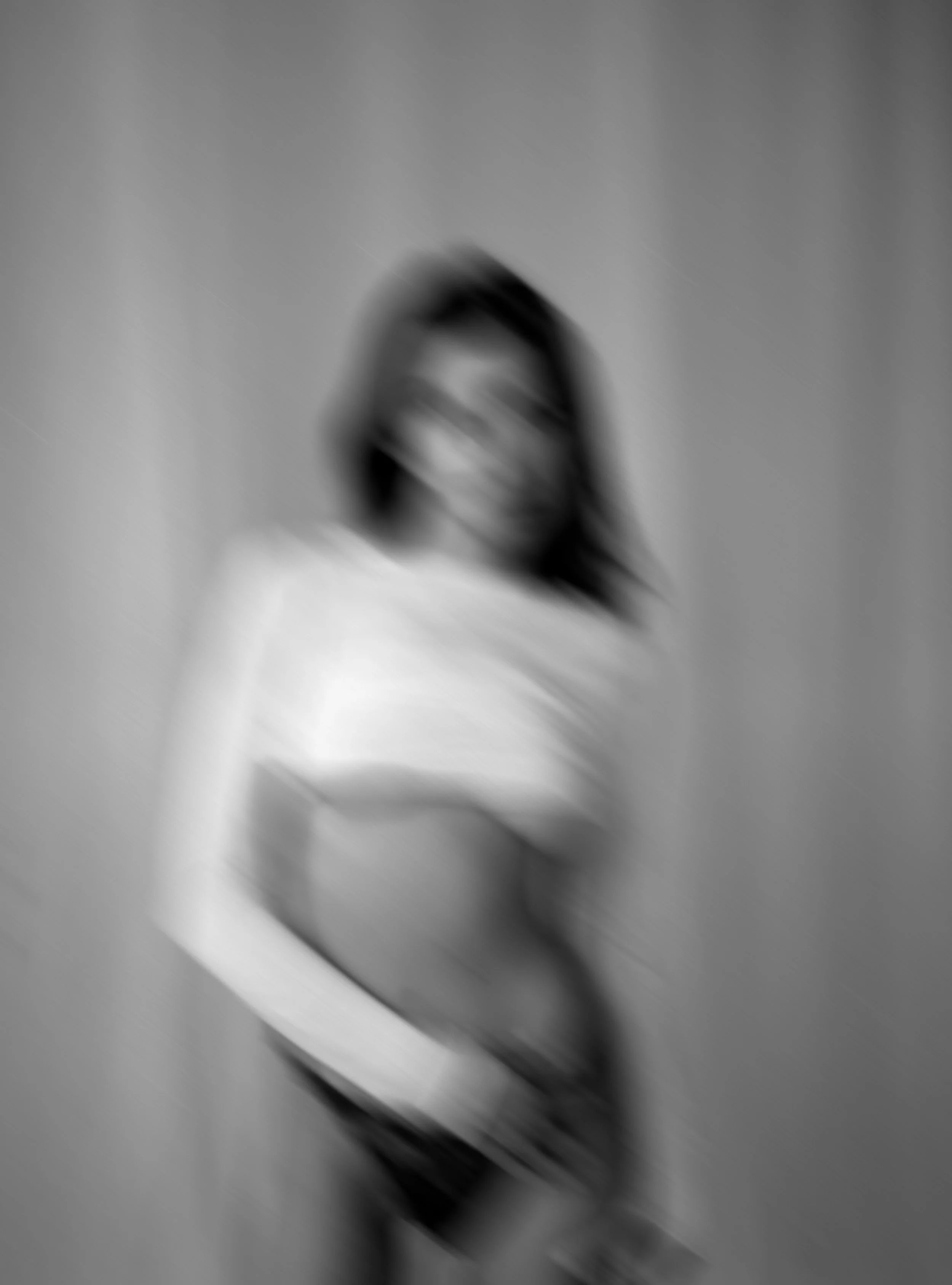 Eine verschwommene Schwarz-Weiß-Fotografie einer Frau, die lachend in die Kamera schaut, vor einem neutralen Hintergrund.