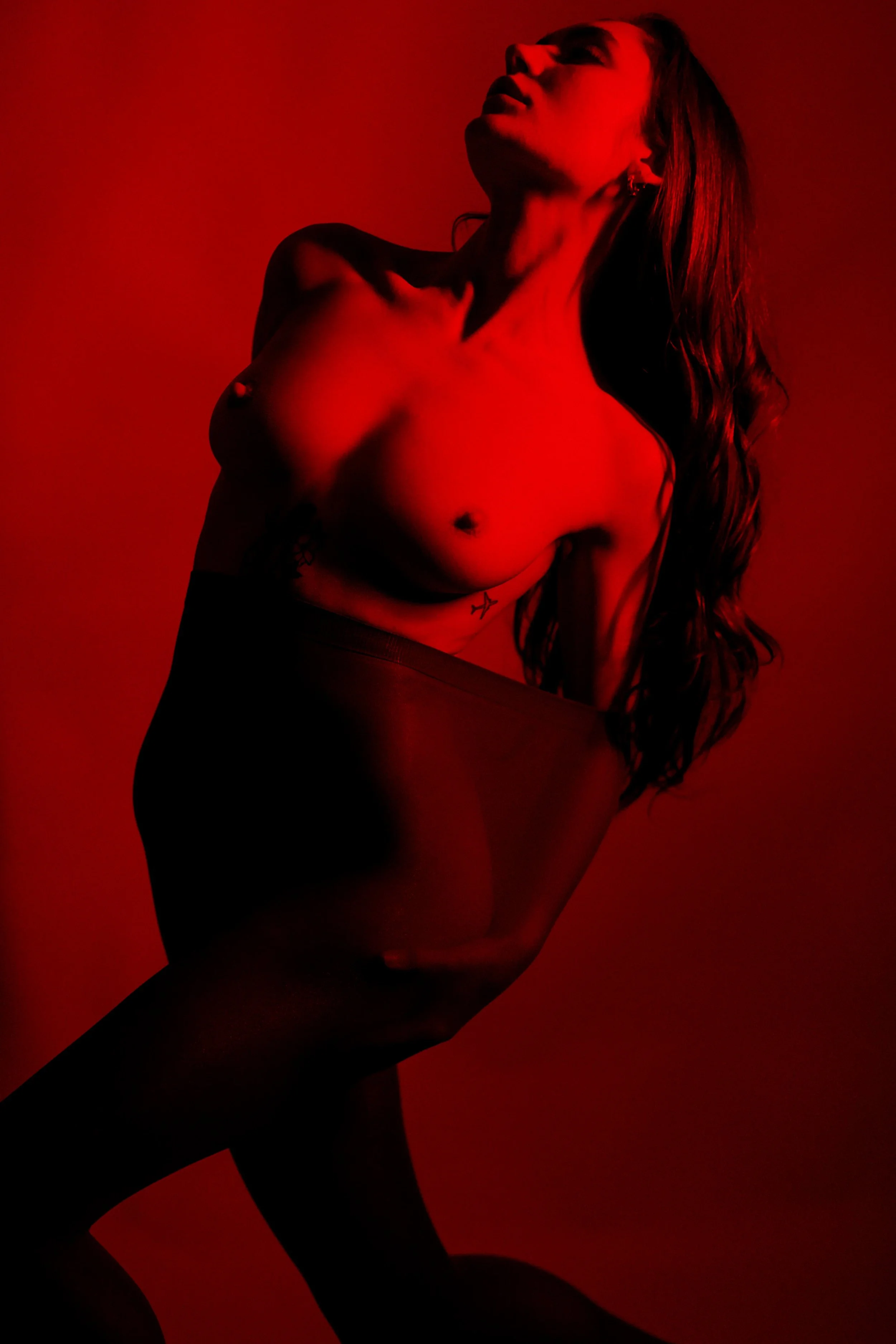 Eine nackte Frau mit langen Haaren, die gegen eine rote Hintergrund lehnt.