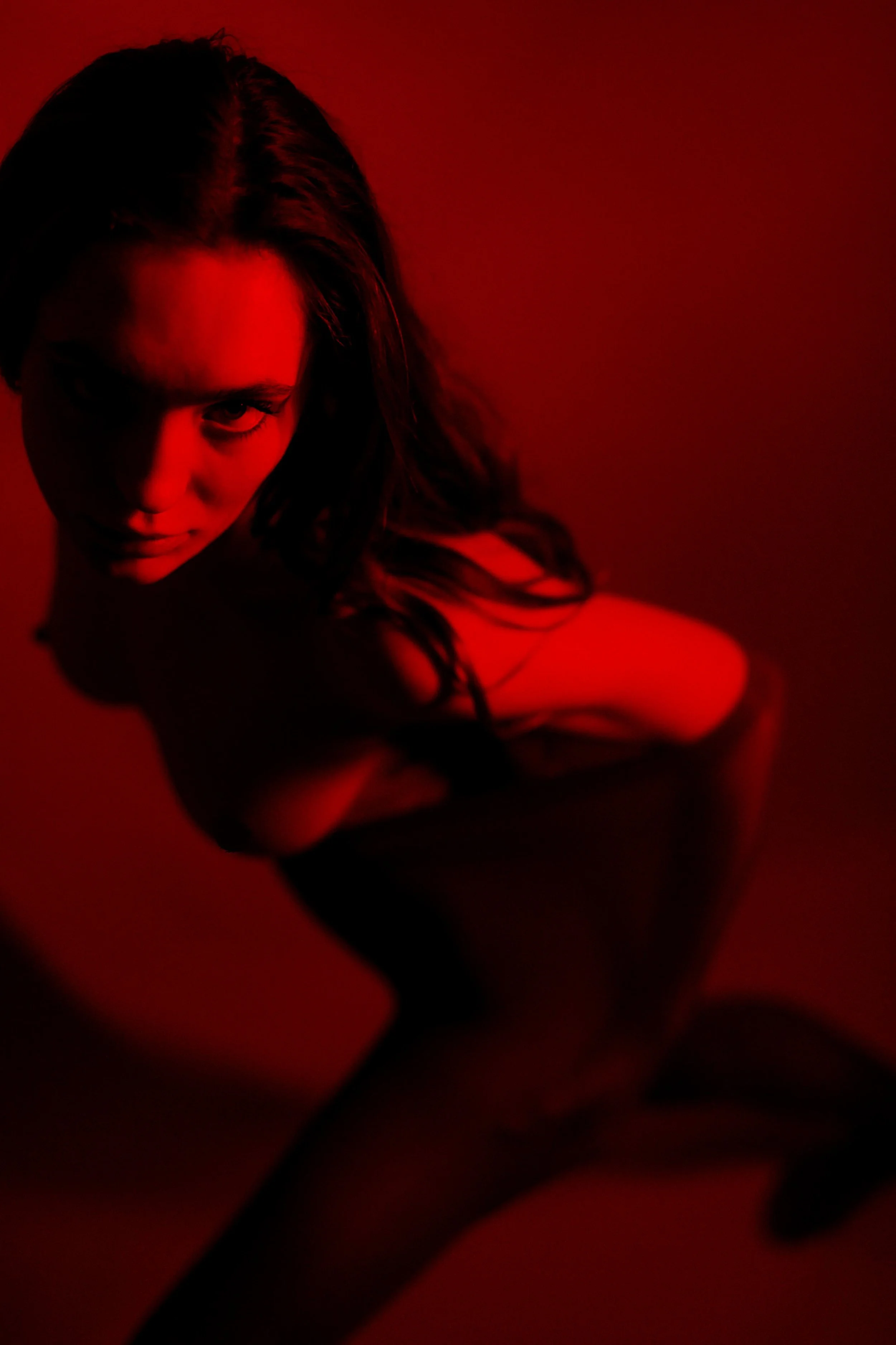 Junge Frau in schwarzem Kleid, die auf einem roten Hintergrund kniet und in die Kamera blickt.