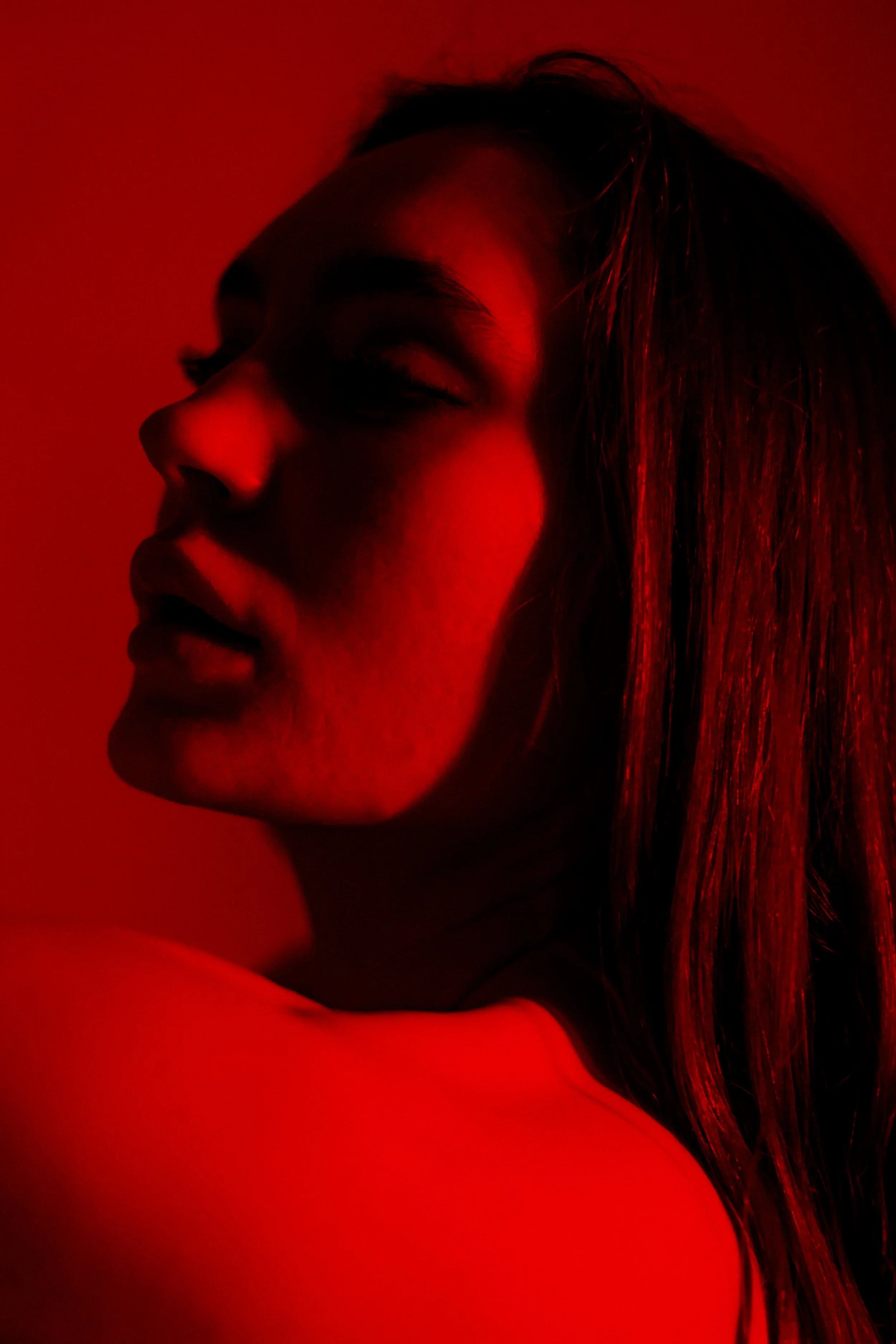 Porträt einer Frau, die im roten Licht leuchtet, mit geschlossenen Augen und einer nachdenklichen Stimmung.