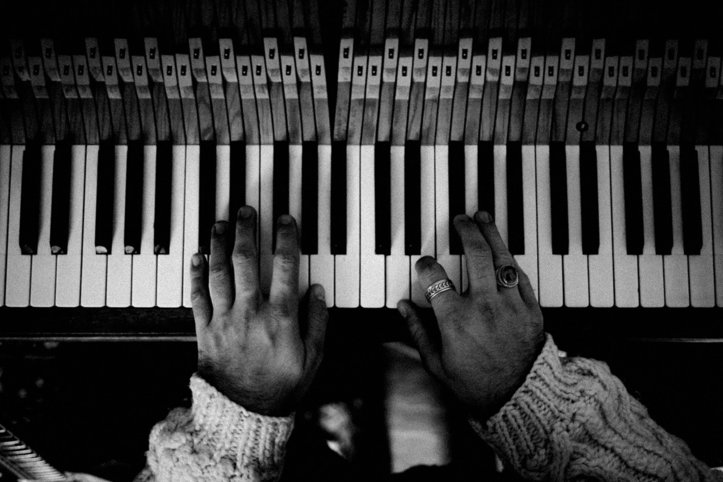 Pianospieler mit beiden Händen auf Tasten, Hands wearing rings und einer Strickjacke.