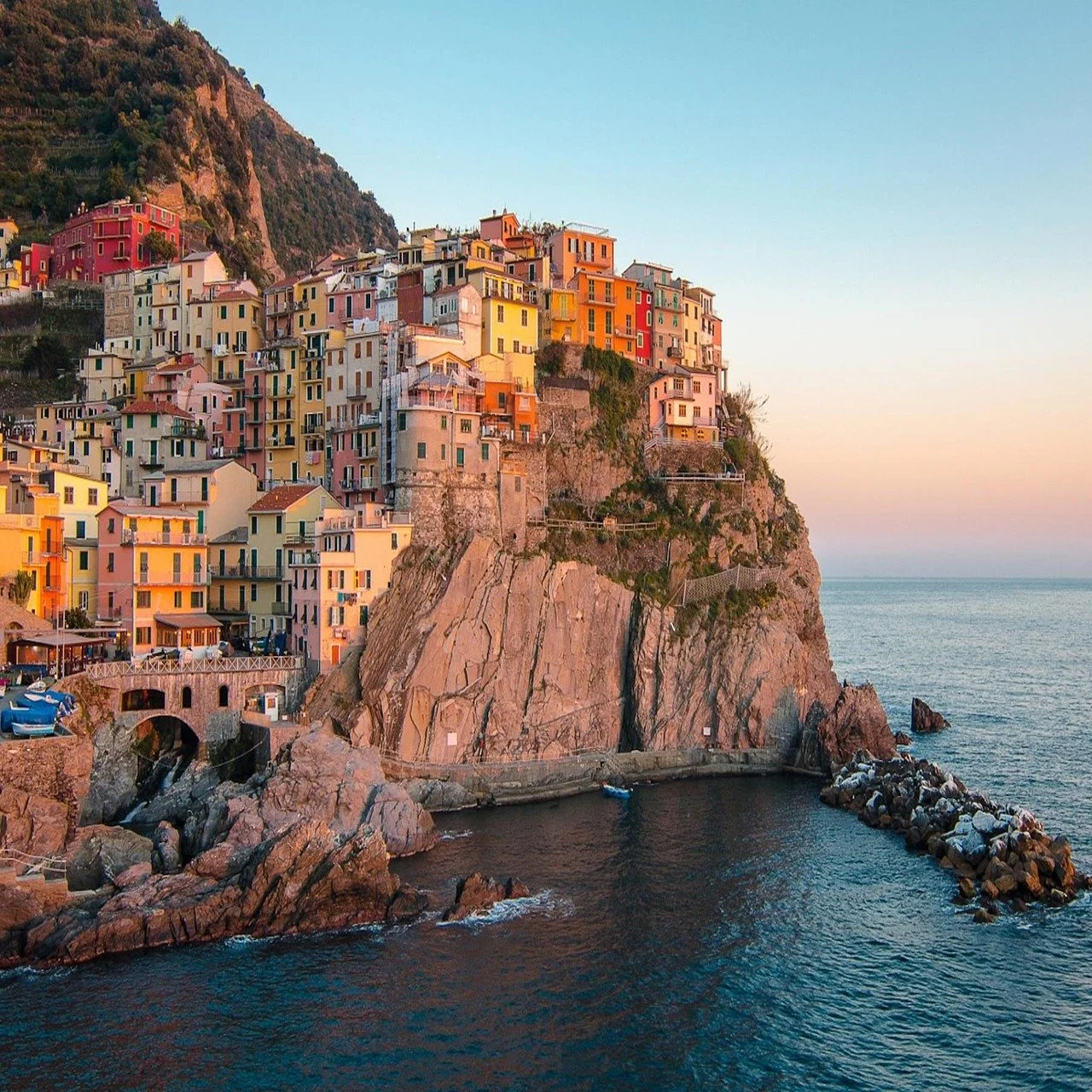 Colorful houses on a cliff overlooking the ocean during sunset.