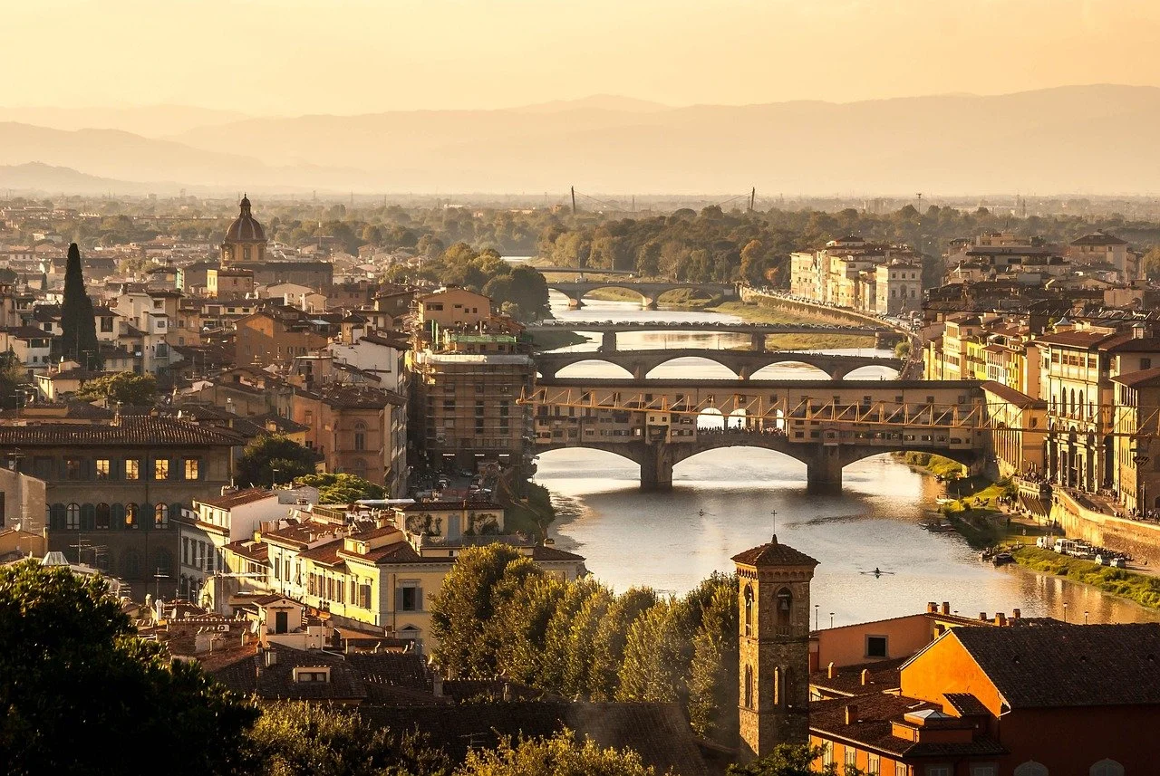 A cityscape with multiple bridges crossing a river during sunset, with buildings, trees, and hills in the background.