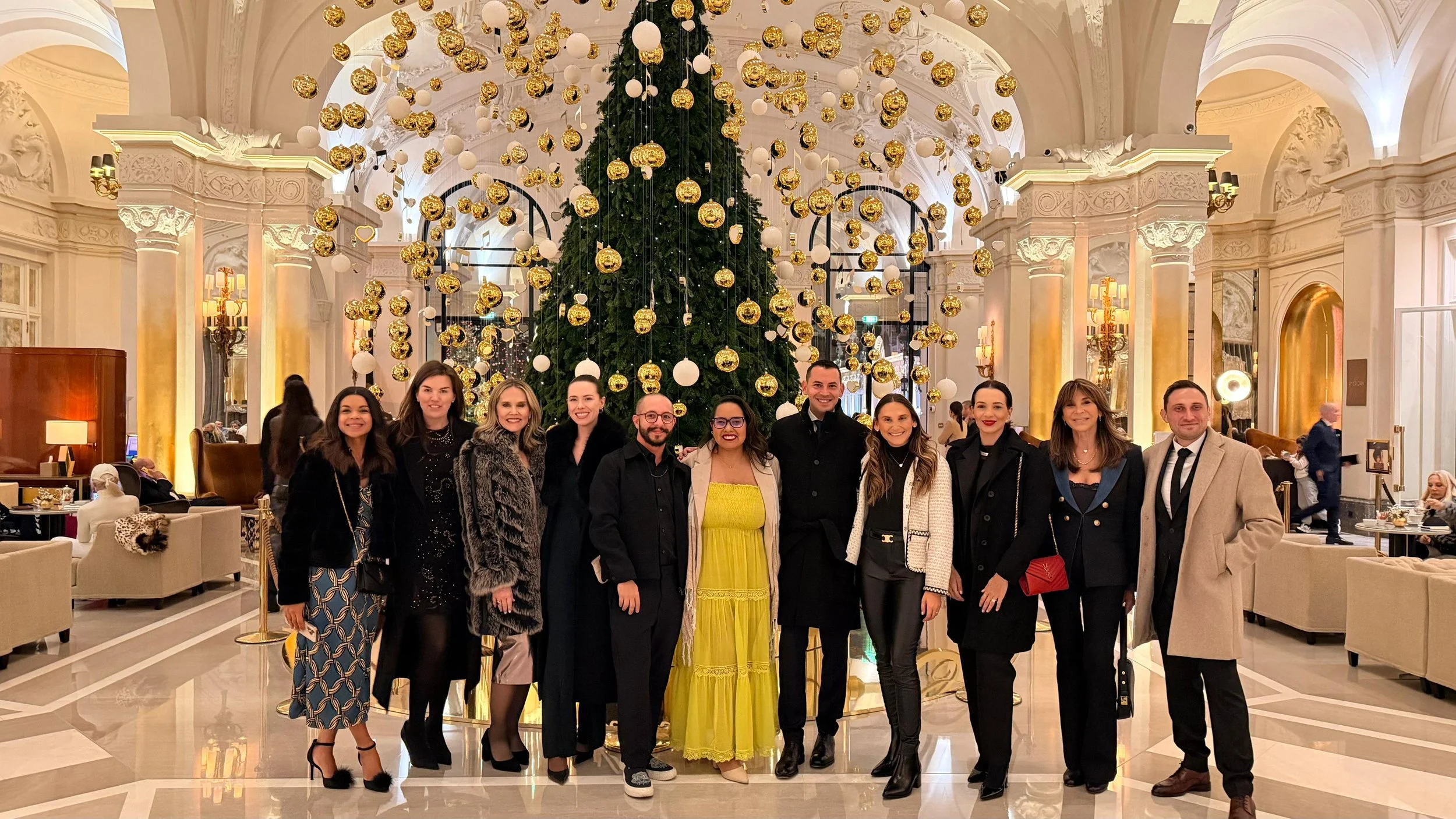 Group of ten people posing in front of a decorated Christmas tree in an elegant hotel lobby.