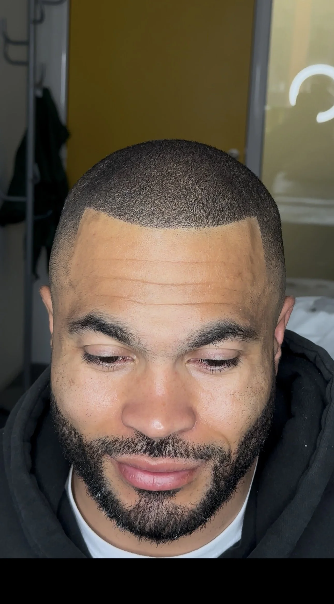 Un homme avec une coupe de cheveux très courte, vu de face, avec un fond flou.