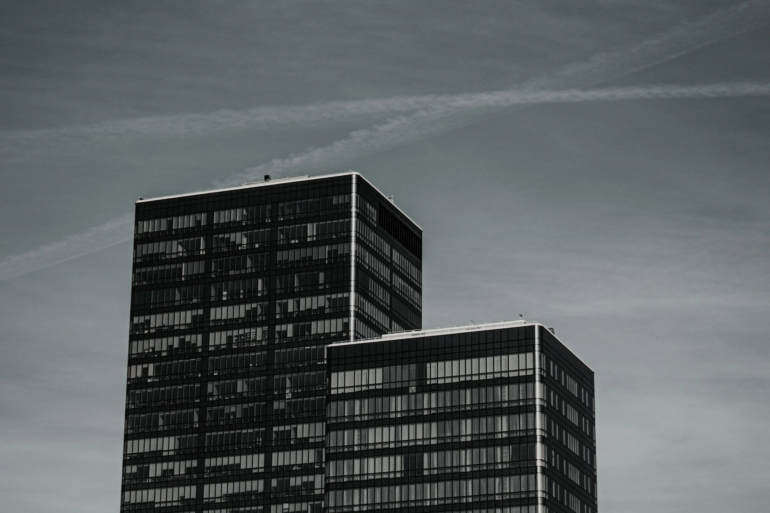 Zwei moderne Wolkenkratzer mit dunklen Glasfassaden unter einem bewölkten Himmel.