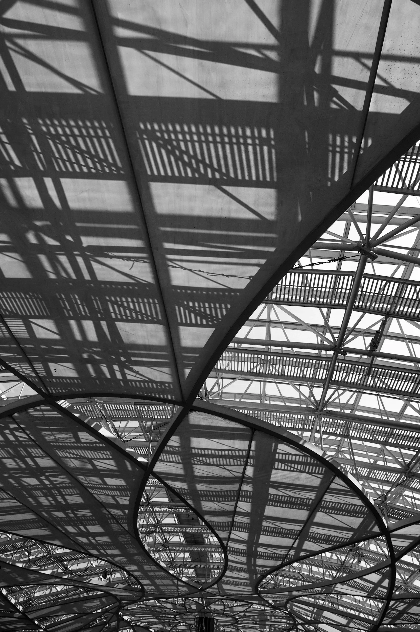 Schattenspiele und Schatten von Treppen und Metallstrukturen an einer modernen Gebäudedecke in schwarzer und weißer Fotografie.