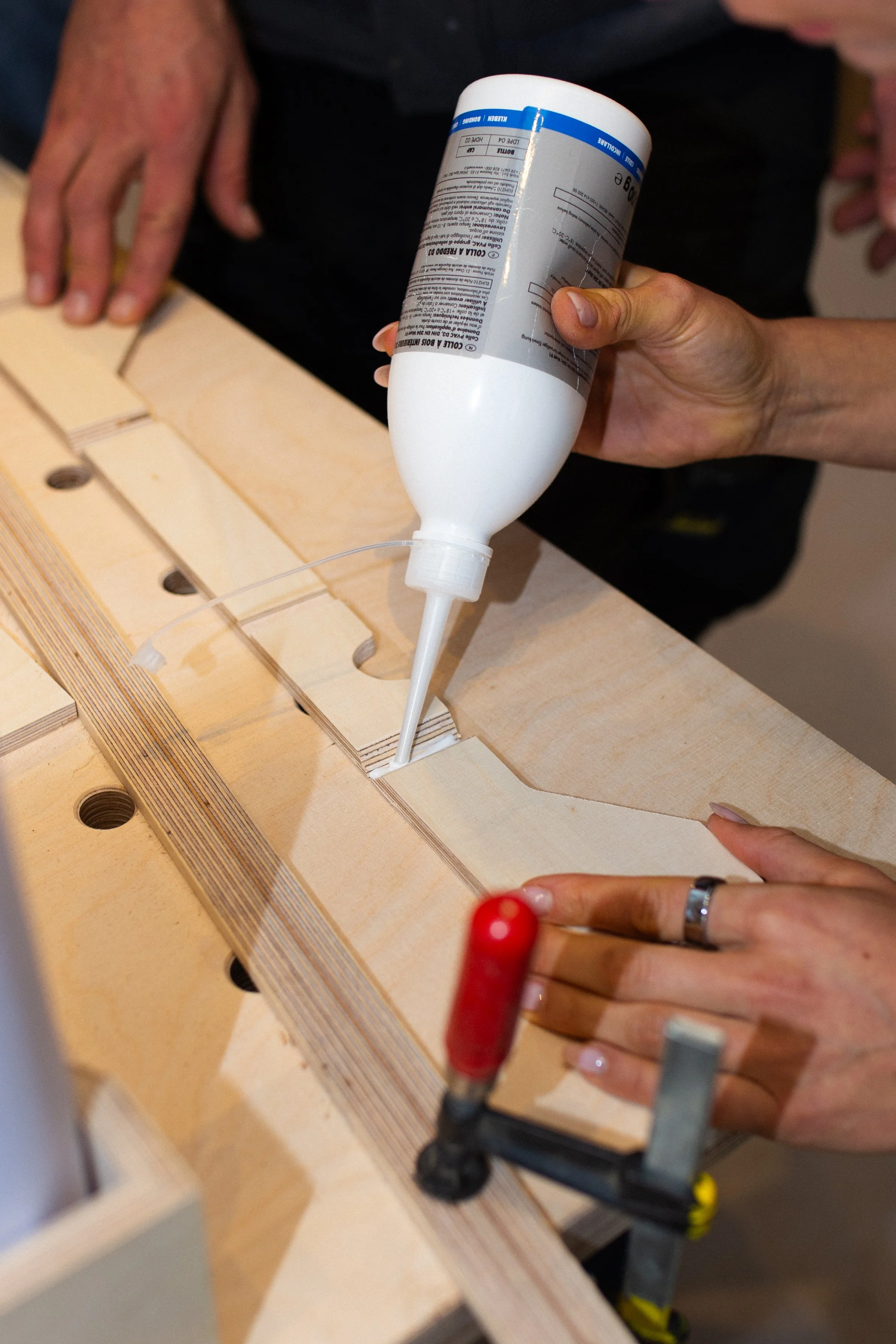 Person verwendet Holzleim, um Holzteile an einem Werkstück zu befestigen, während sie auf einer Werkbank arbeiten.