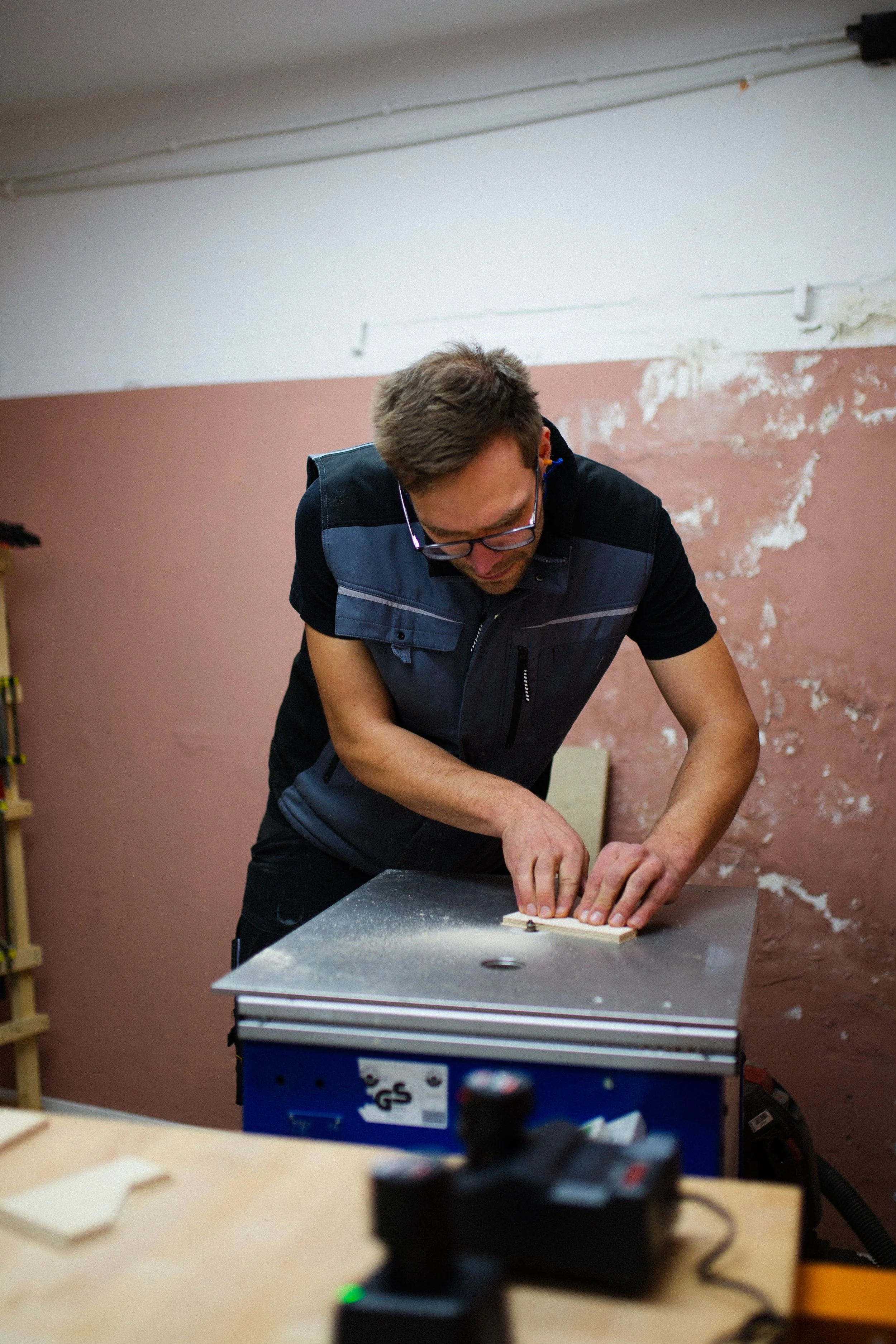 Ein Mann arbeitet an einer Holzplatte in einer Werkstatt, während er auf einem Arbeitstisch steht.