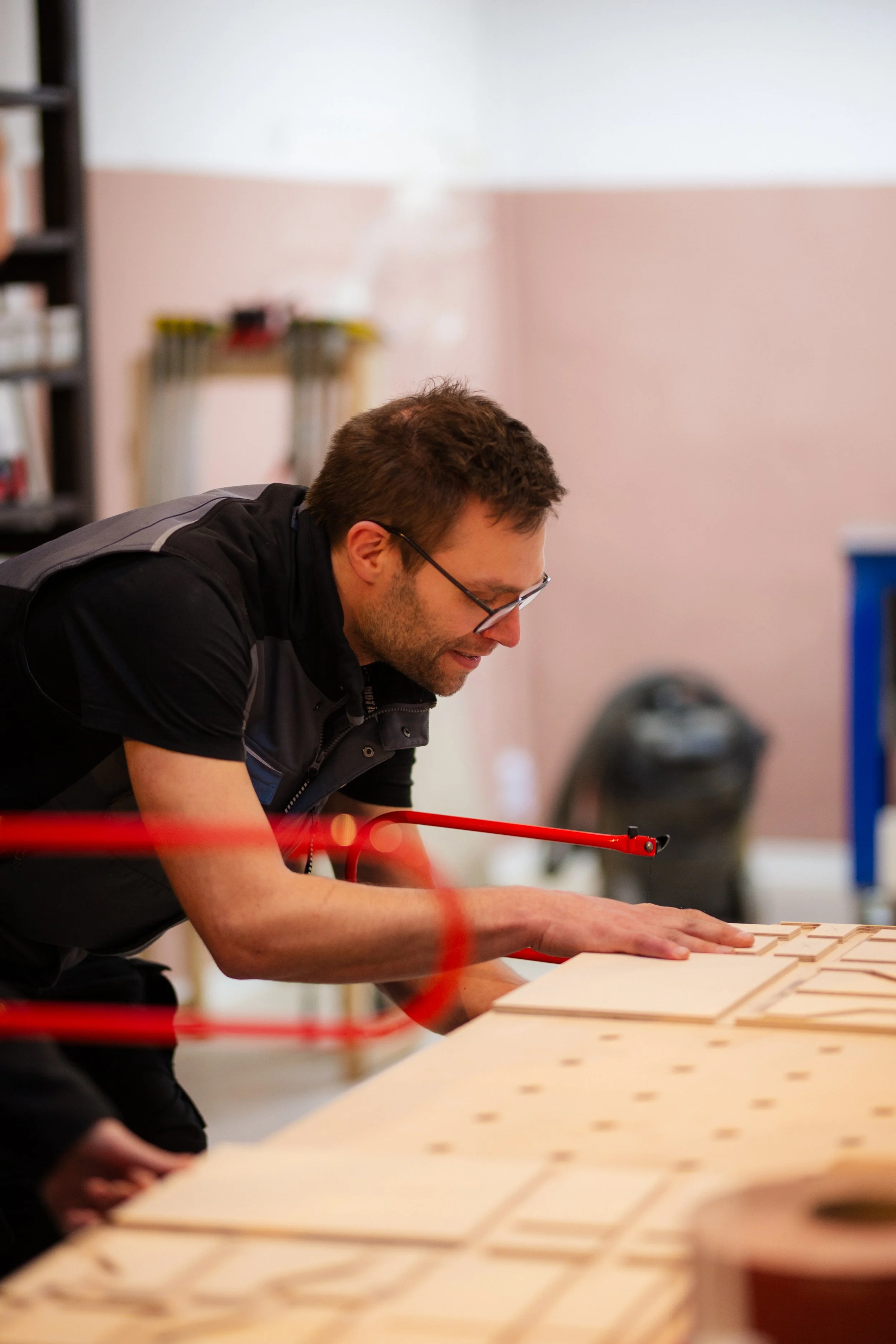 Ein Mann arbeitet in einer Werkstatt an Holzarbeiten, er beugt sich über eine große Holzplatte mit ausgeschnittenen Mustern.