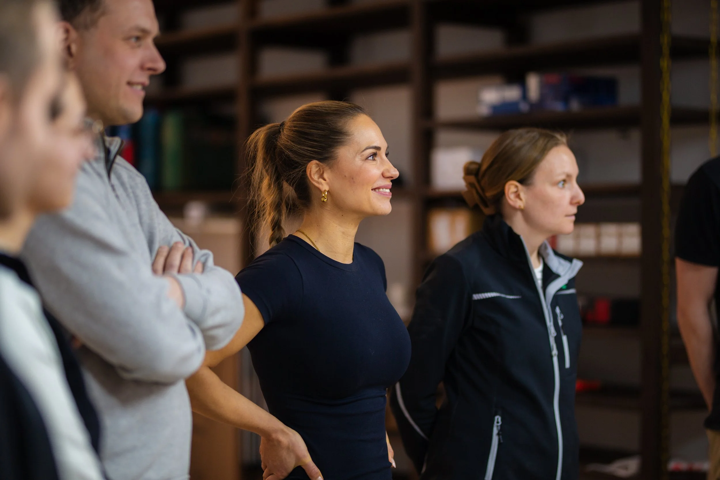 Gruppe von Menschen, die in einer Halle stehen, aufmerksam und lächelnd, möglicherweise bei einem Trainings- oder Workshops-Event.
