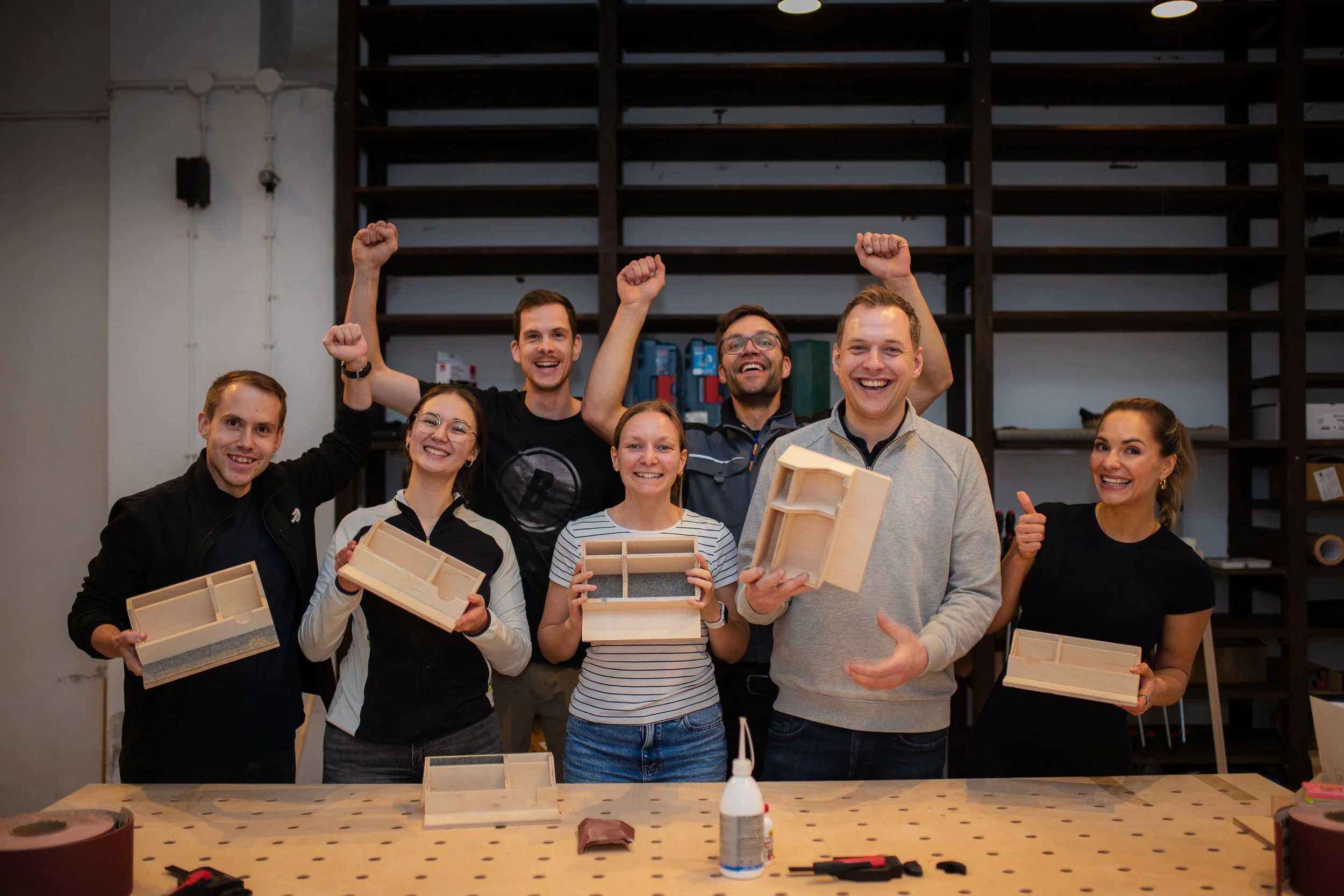 Eine Gruppe von Menschen bei einem Workshop, die Holzboxen hält und feiert.