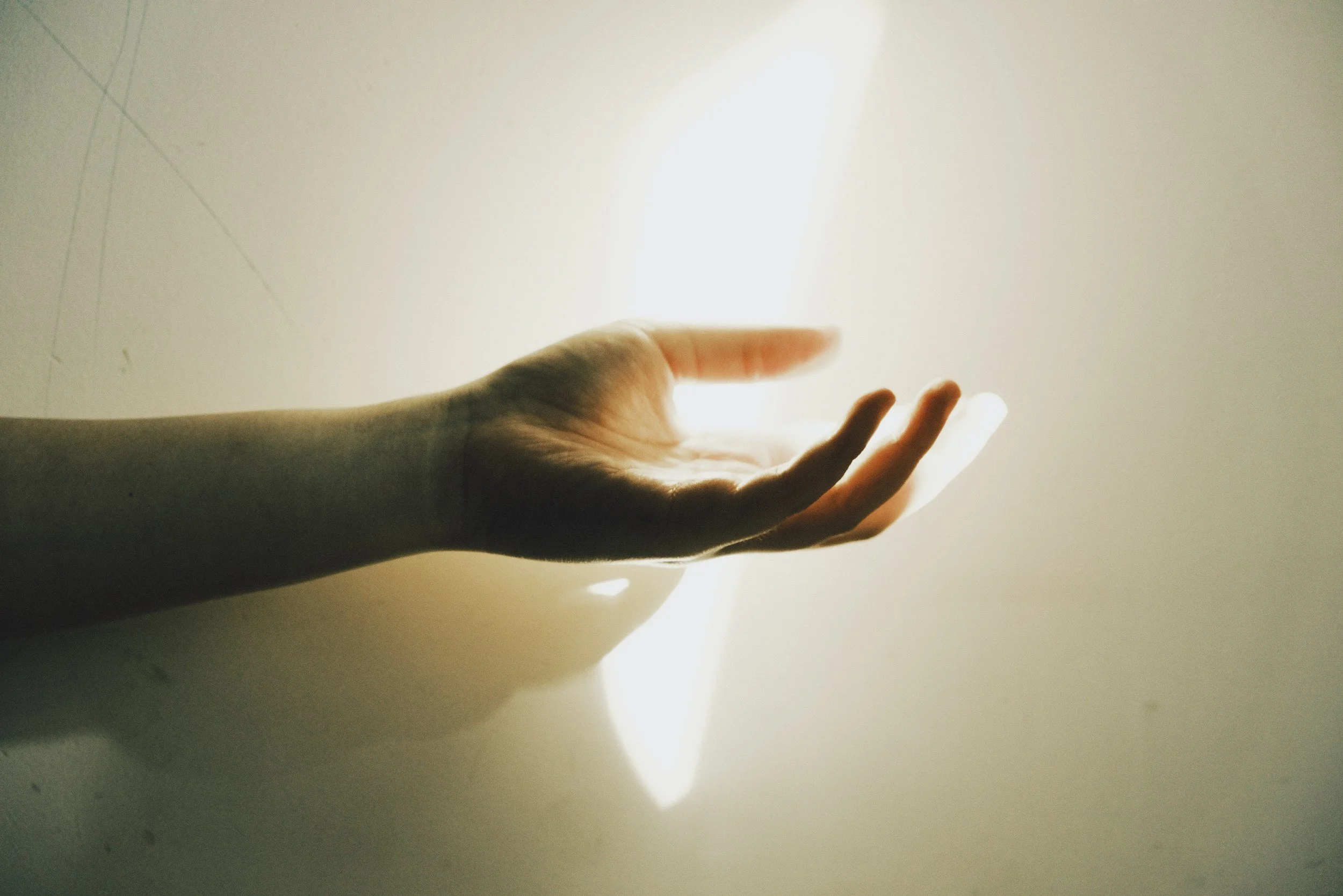A human hand reaching out towards bright light against a plain background.