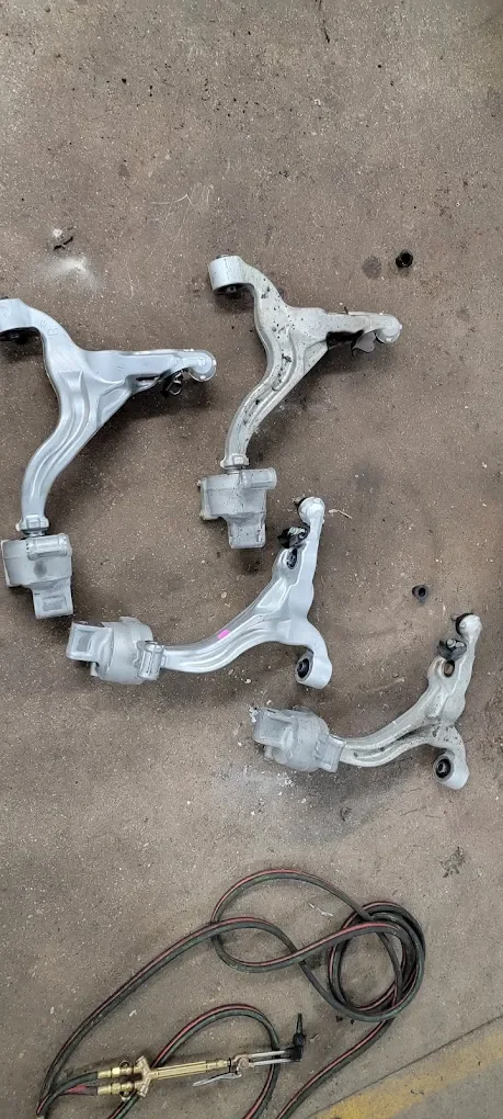 Three automotive control arms and a set of electrical wires with a connector on a concrete floor.