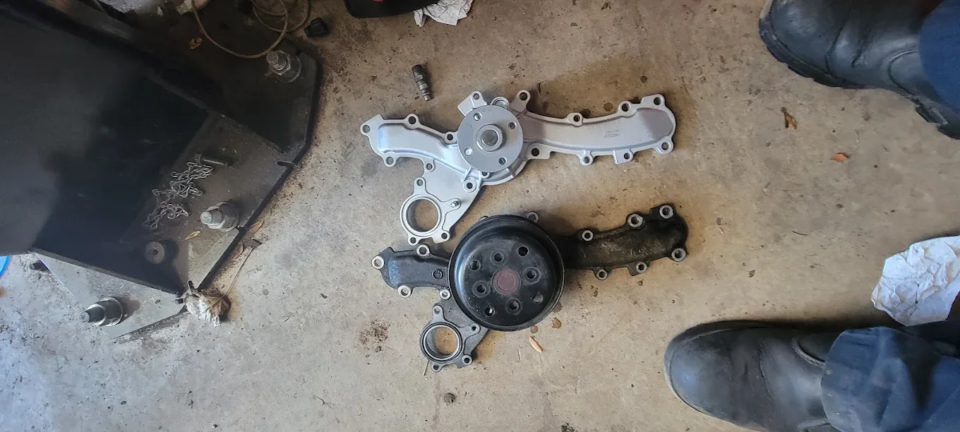 Car water pump and timing cover lying on garage floor.