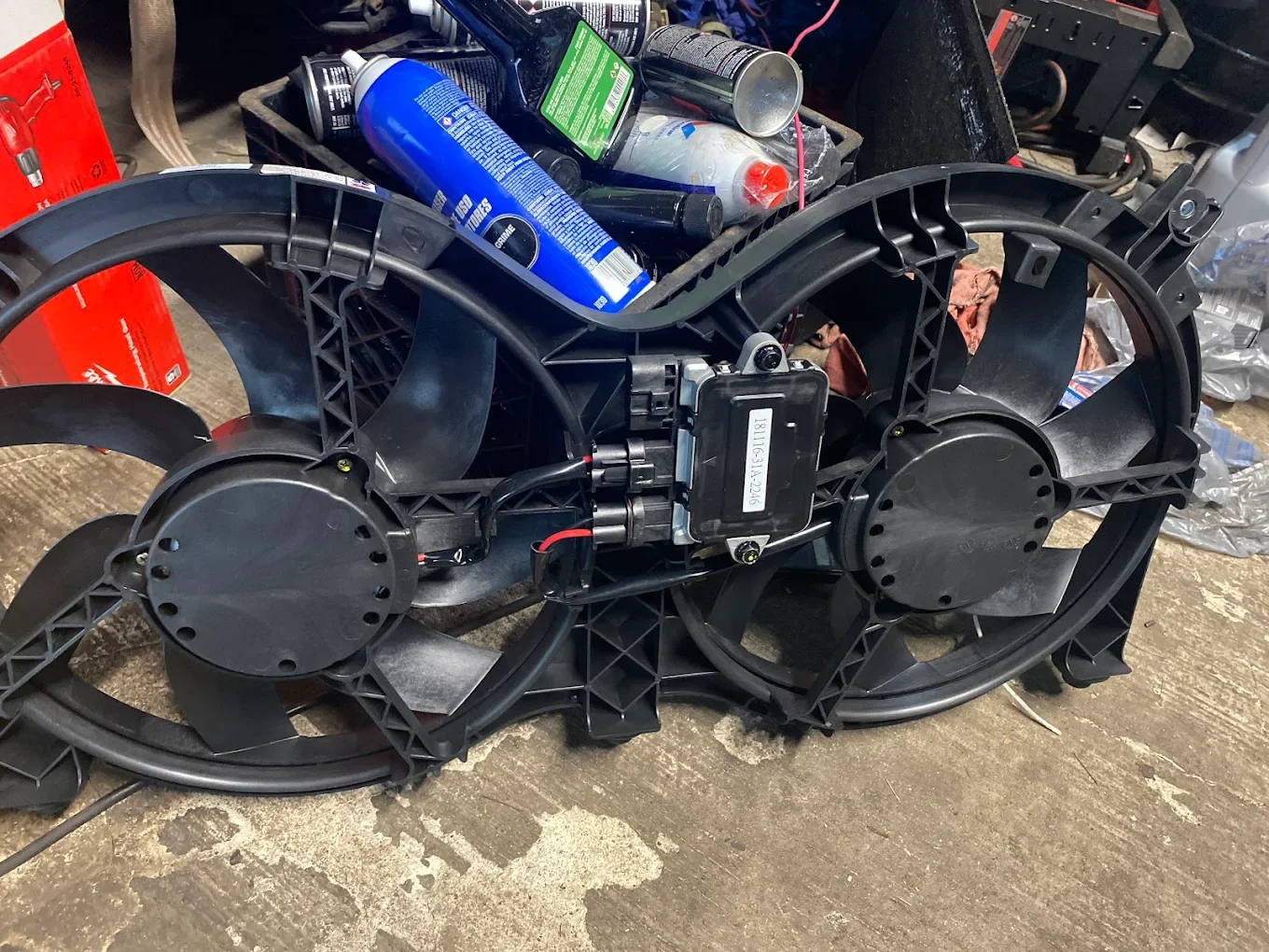 A disassembled electric motorcycle frame with wheels, motor, and electronic components, placed on a concrete floor with tools and supplies in the background.