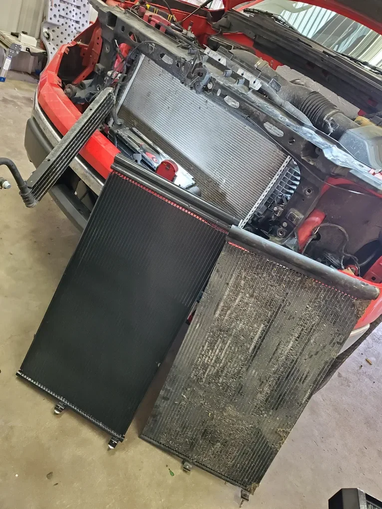 A car with its front end disassembled, showing three radiators or intercoolers propped against the bumper and a work area in the background.